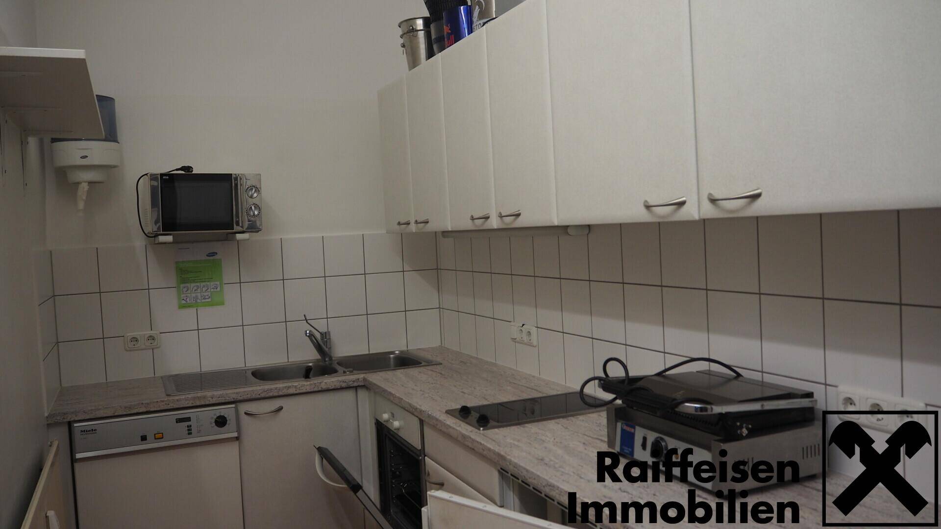 Funktionale Küche mit weißen Schränken, Edelstahlspüle und Mikrowelle, ideal für den Gastronomiebetrieb.