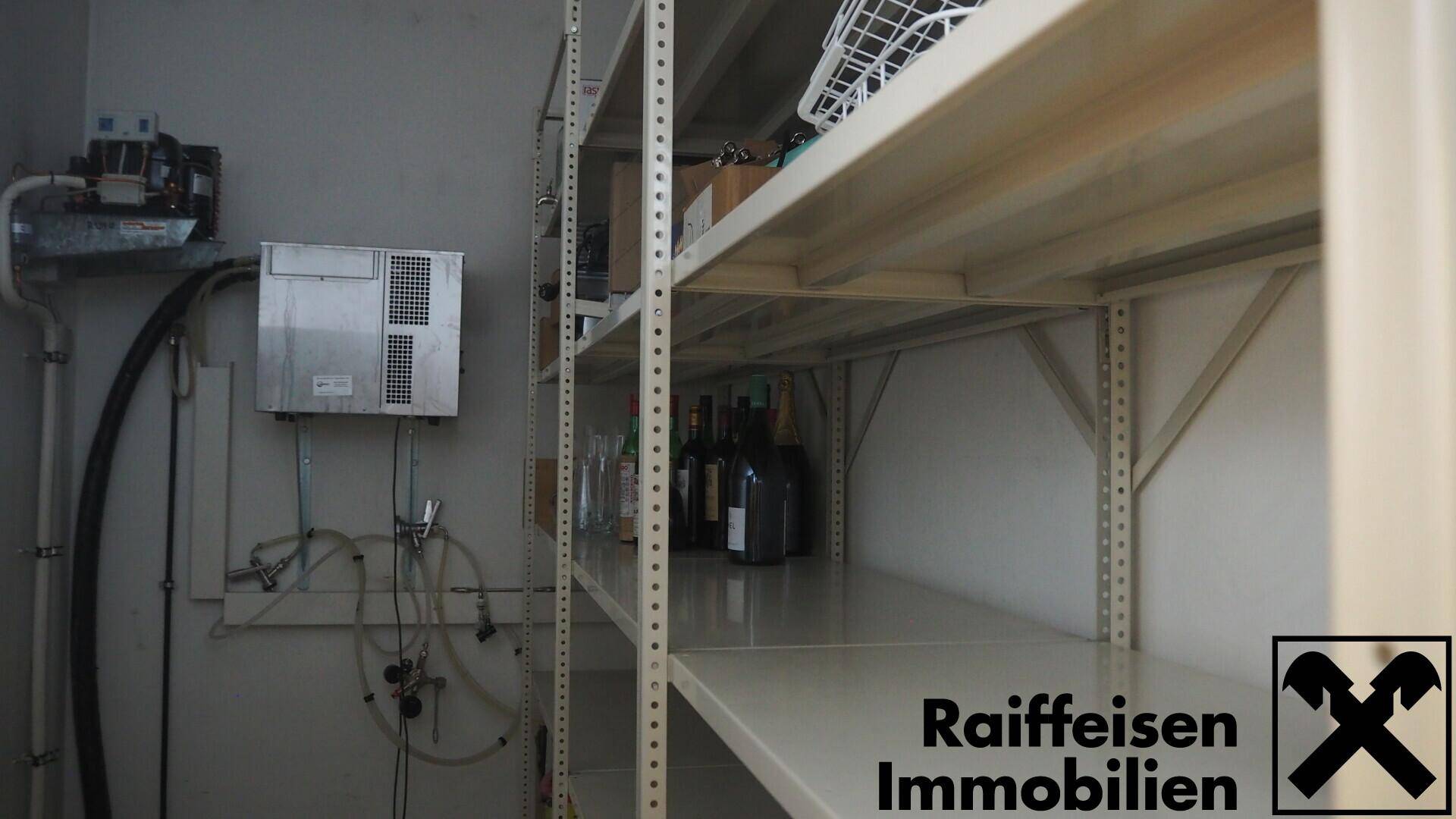 Lagerraum mit Metallregalen und gelagerten Flaschen, ausgestattet mit technischen Installationen an der Wand.