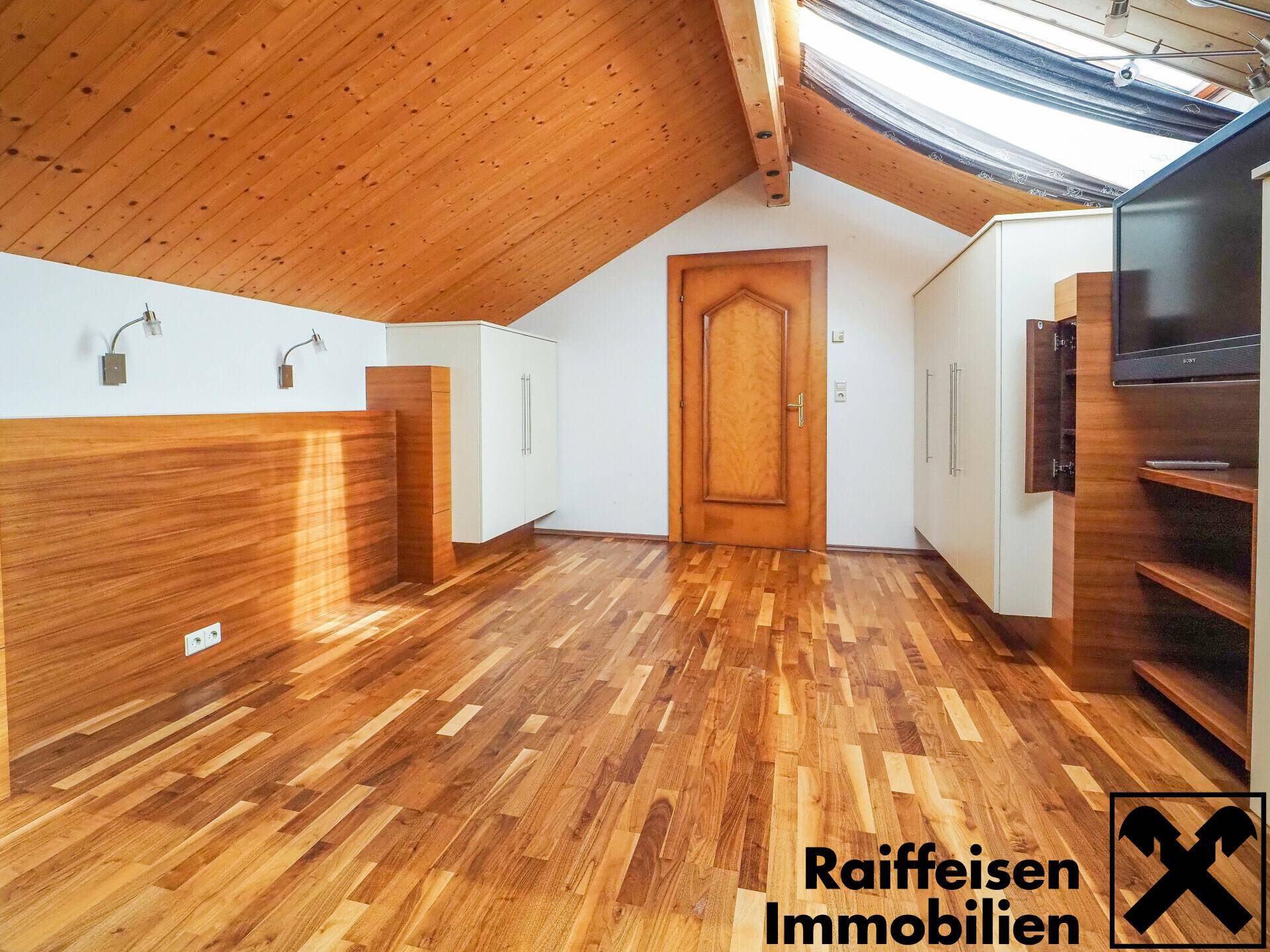 Heller Raum mit Holzboden, Holzdecke und Dachschrägen, durchflutet von natürlichem Licht.