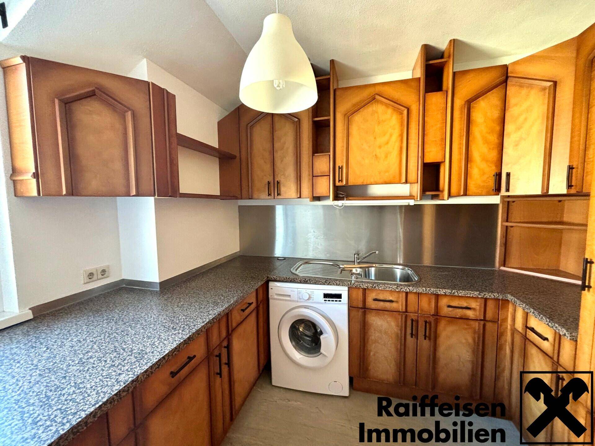 Funktionale Küche mit Holzschränken, dunkler Arbeitsplatte und integrierter Waschmaschine.