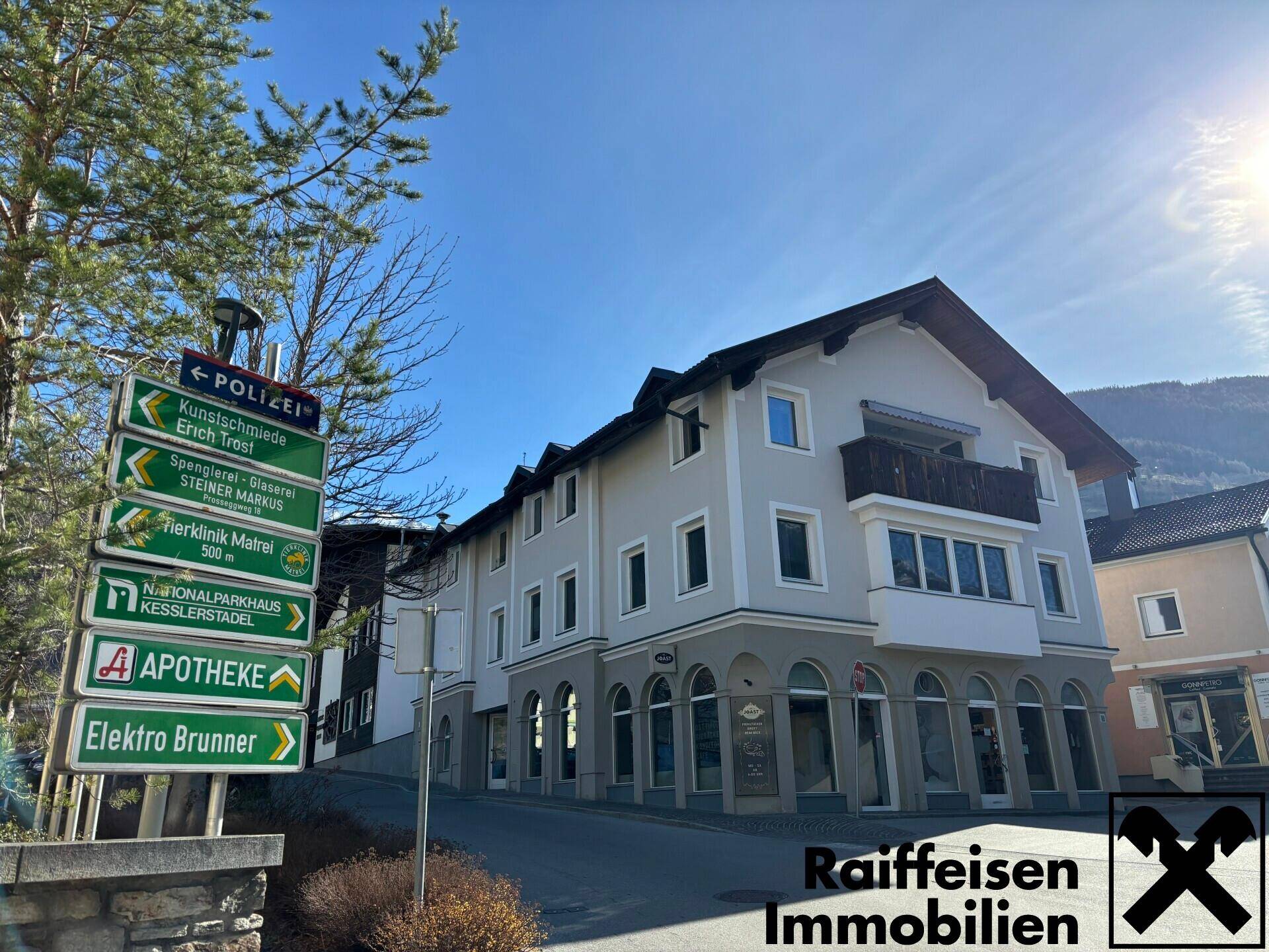 Mehrstöckiges Gebäude an einer Straße mit Geschäften im Erdgeschoss und einem Wegweiser.