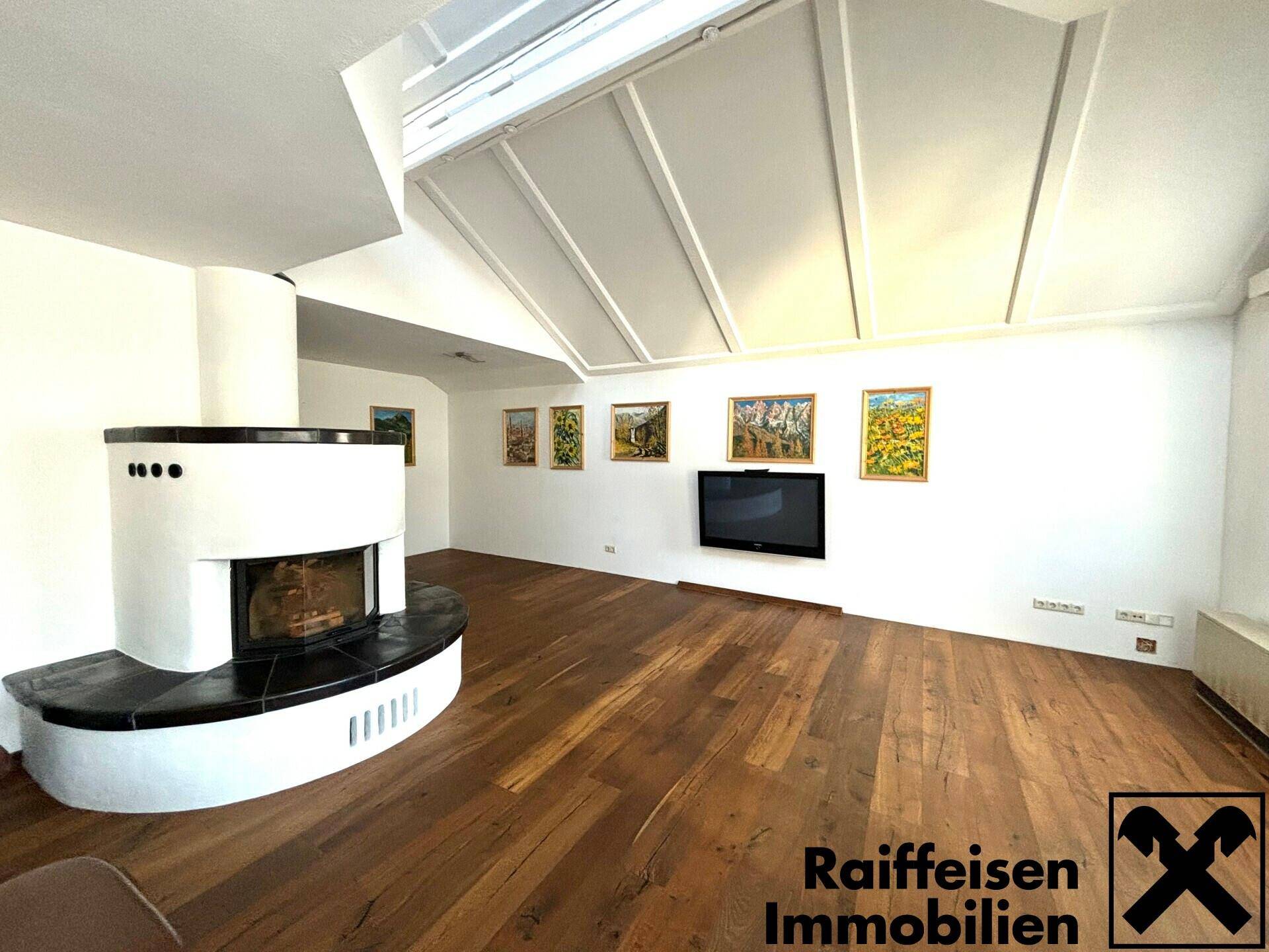 Heller Wohnbereich mit elegantem Kamin, Holzboden und großen Dachfenstern, die viel Licht hereinlassen.