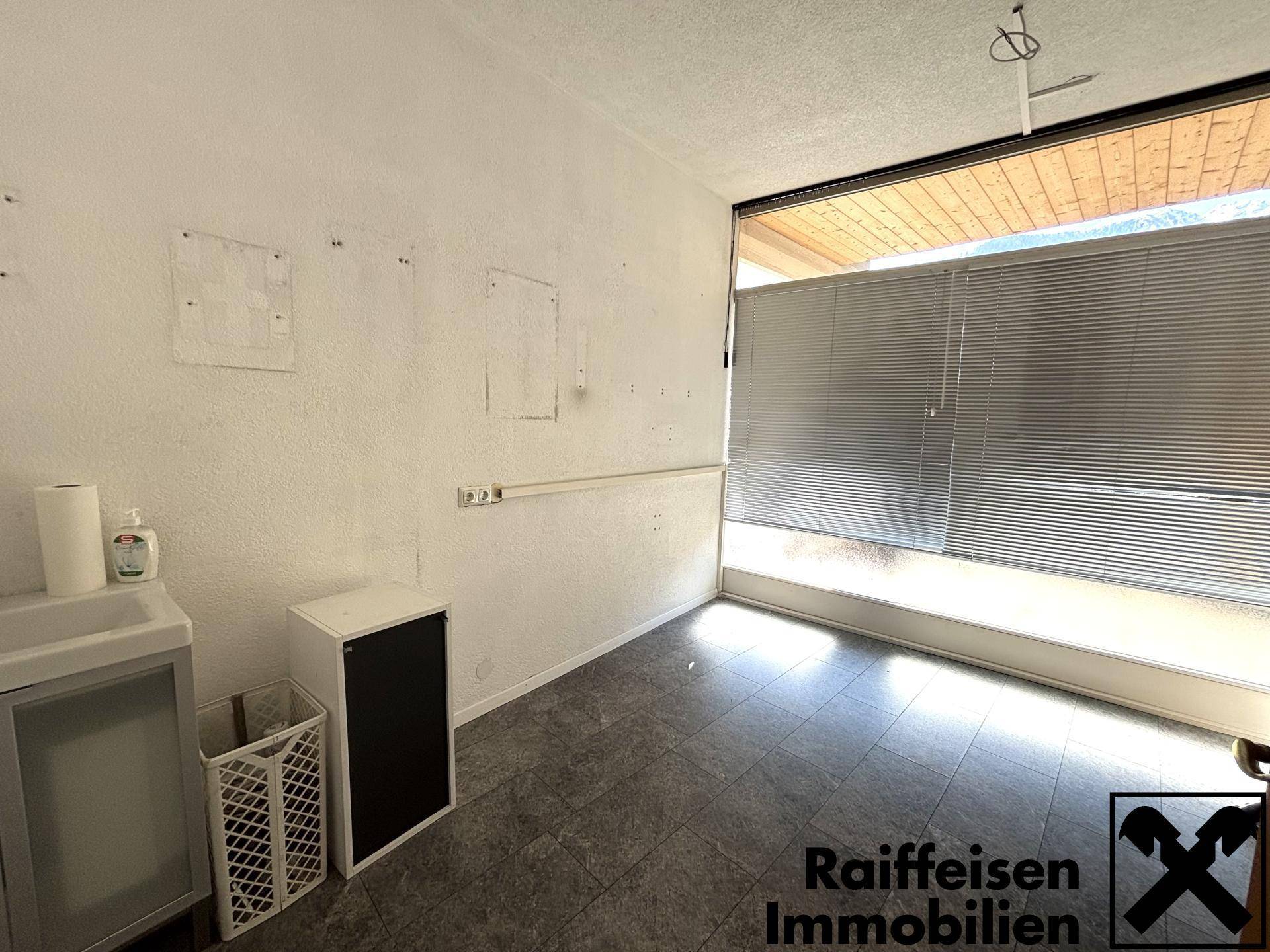 Funktionaler Hauswirtschaftsraum mit Waschbecken und dunklem Fliesenboden, gut beleuchtet durch ein Fenster mit Jalousien.