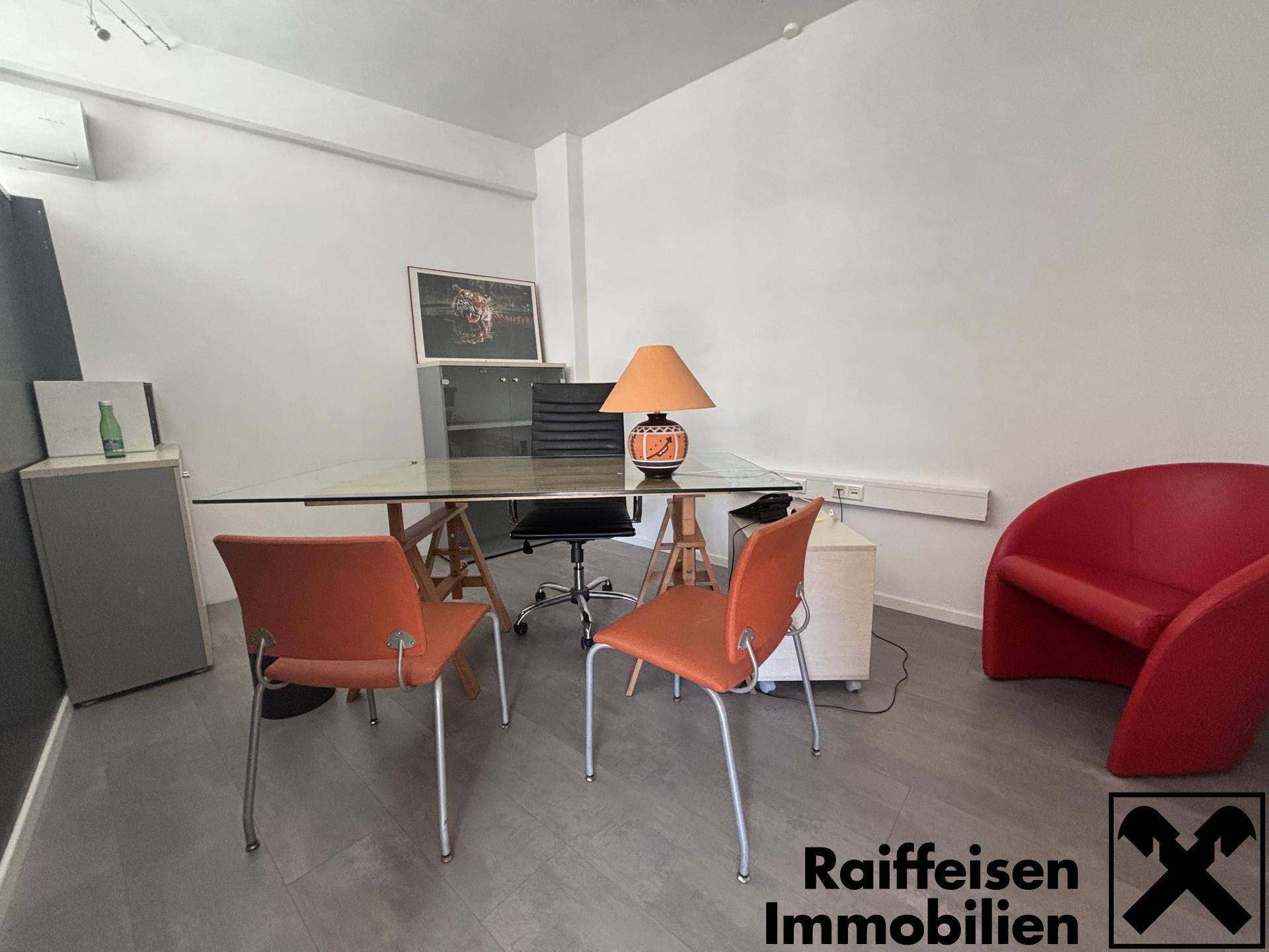 Büro- oder Empfangsbereich mit Glastisch, bequemen Stühlen und einem roten Sessel, hell und modern eingerichtet.