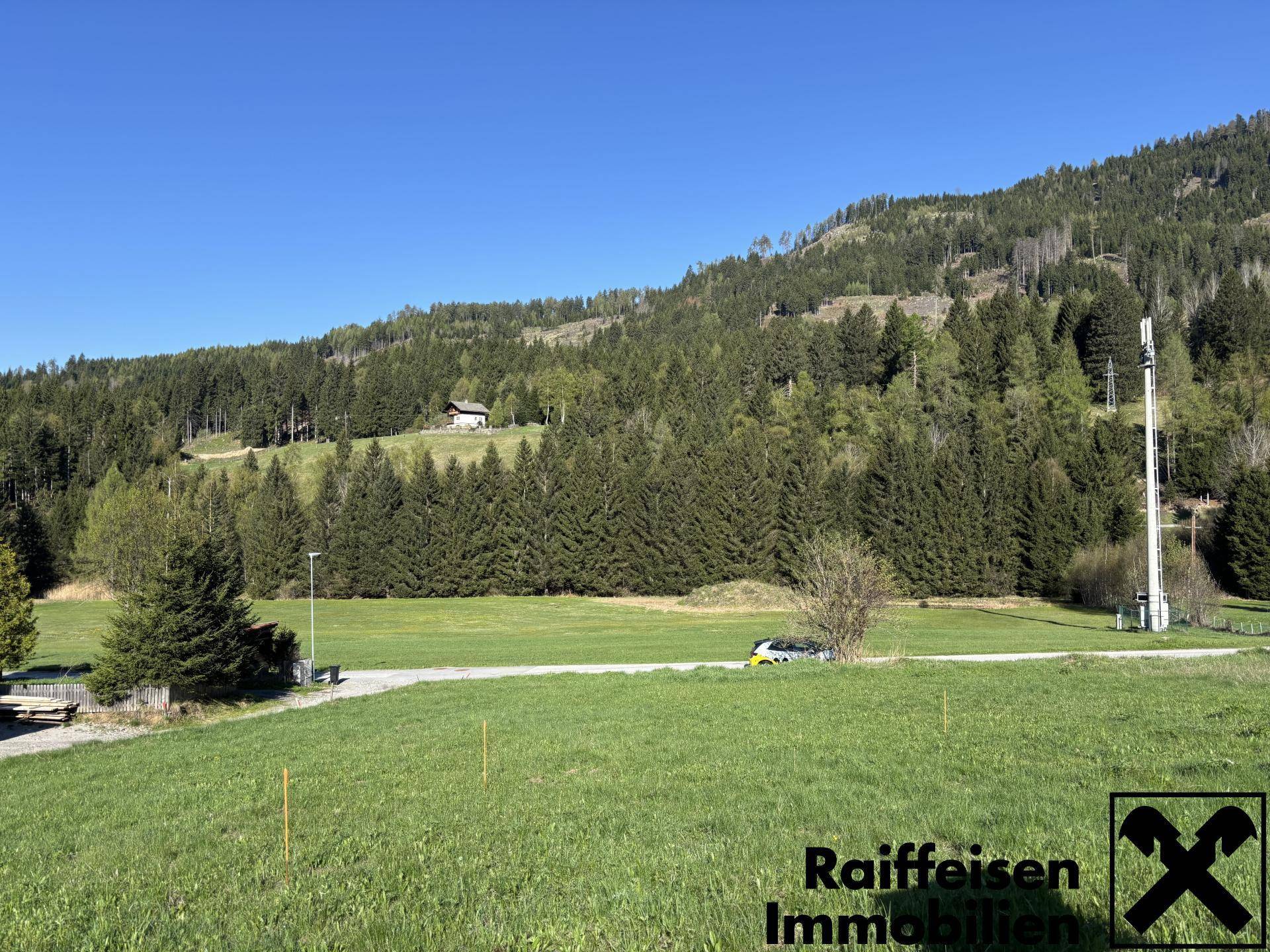 Panoramablick über eine weite grüne Landschaft mit Waldhügeln und einem kleinen Haus in der Ferne.
