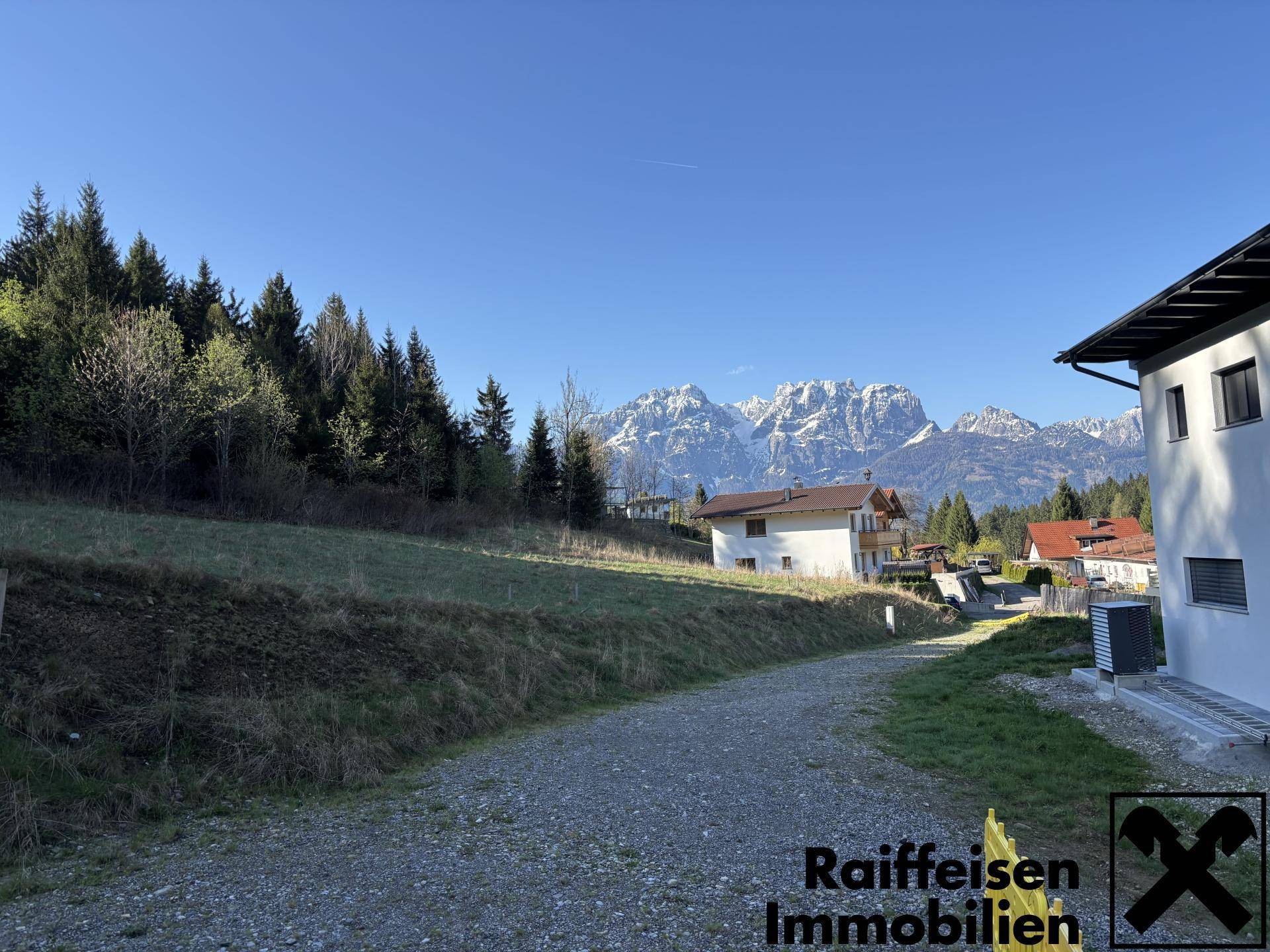 Schotterweg führt zu Häusern mit beeindruckendem Blick auf schneebedeckte Berge in der Ferne.