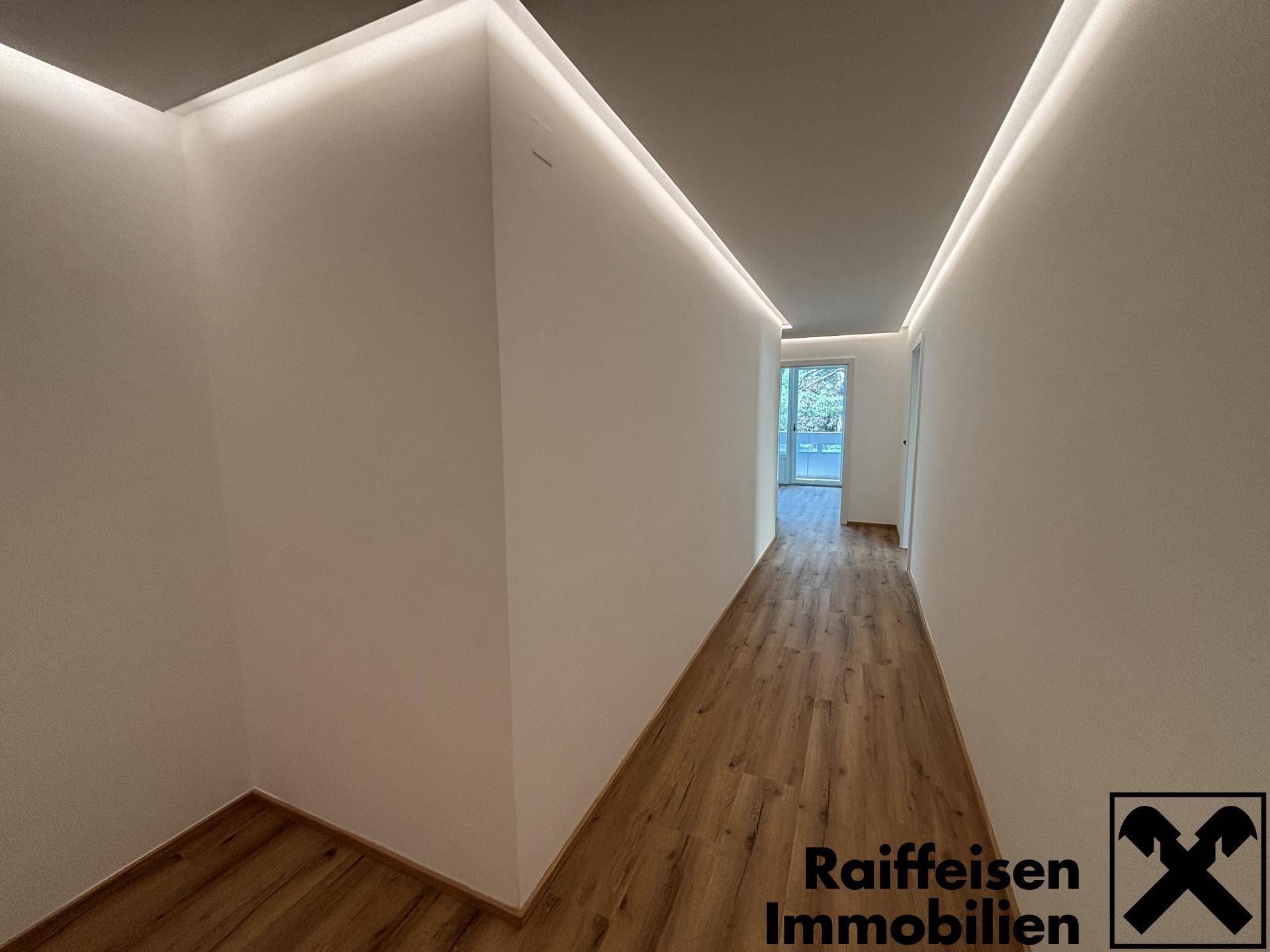 Langer Flur mit Laminatboden und indirekter Beleuchtung, der zu weiteren Räumen führt.
