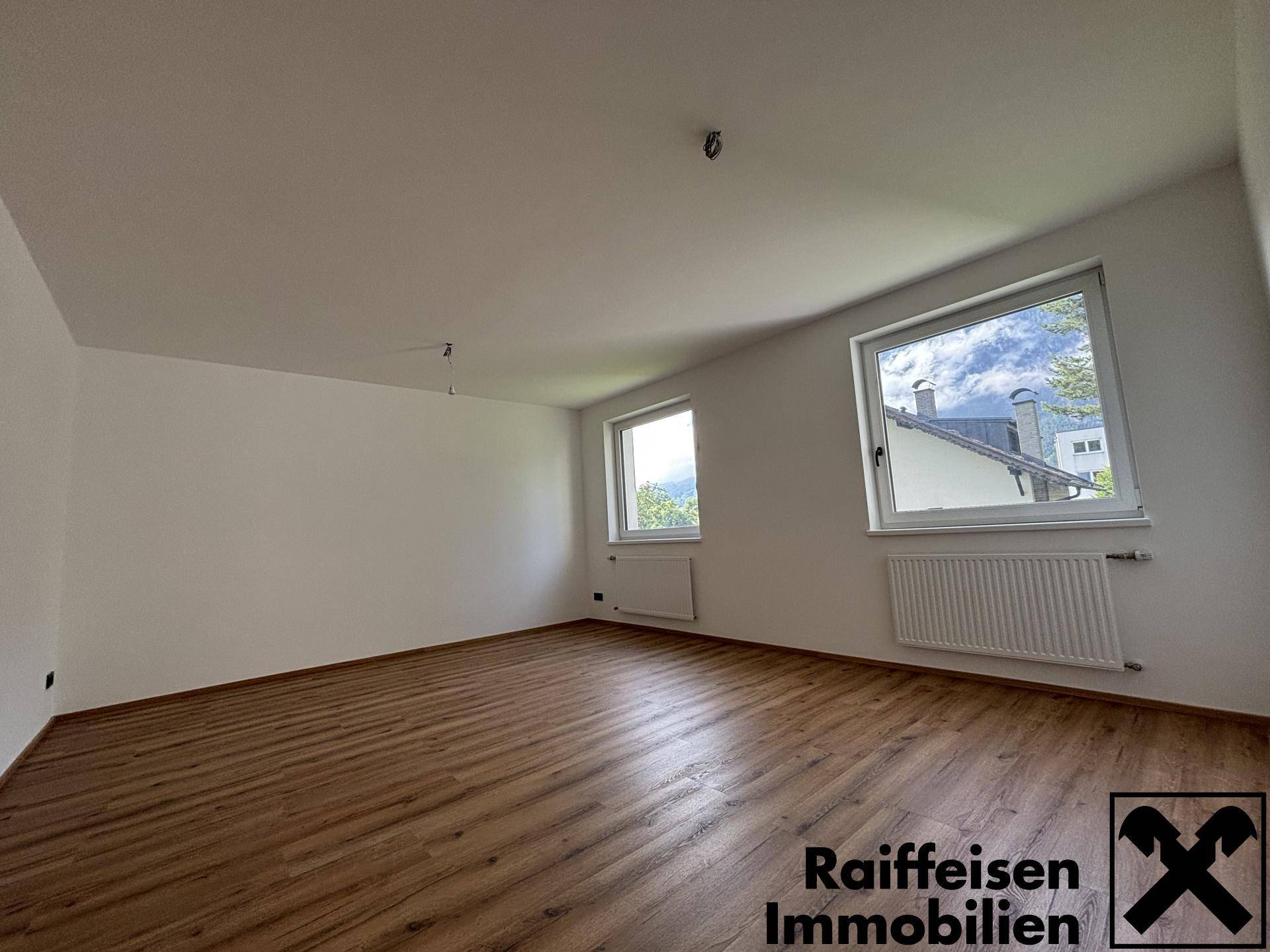 Geräumiges Zimmer mit Laminatboden, hellen Wänden und einem schönen Blick ins Grüne.
