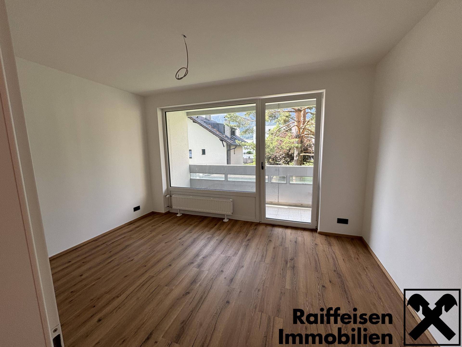 Helles Schlafzimmer mit Laminatboden, weiß gestrichenen Wänden und direktem Balkonzugang.