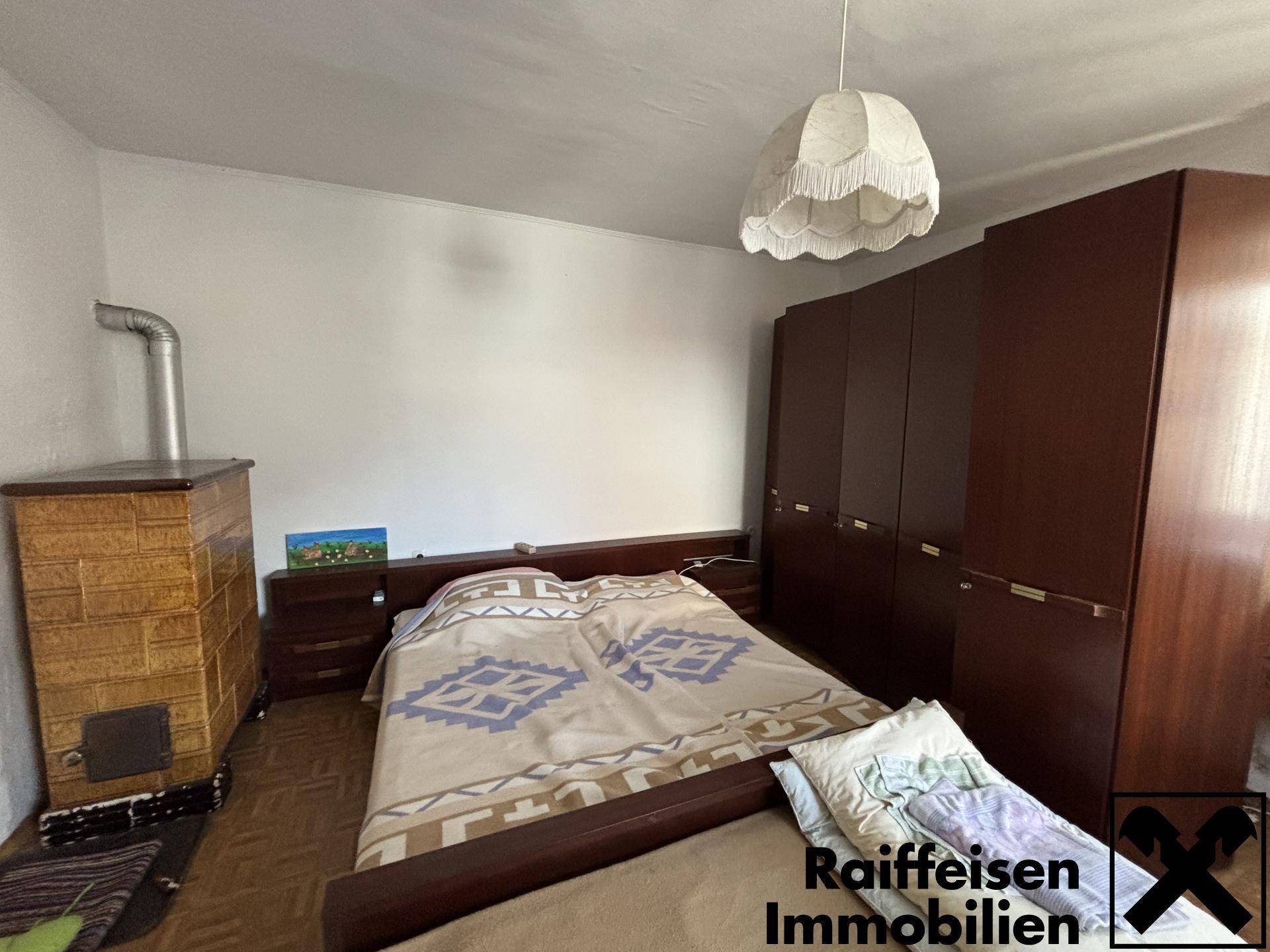 Schlafzimmer mit Doppelbett, Holzschrank und traditionellem Kachelofen für Wärme.