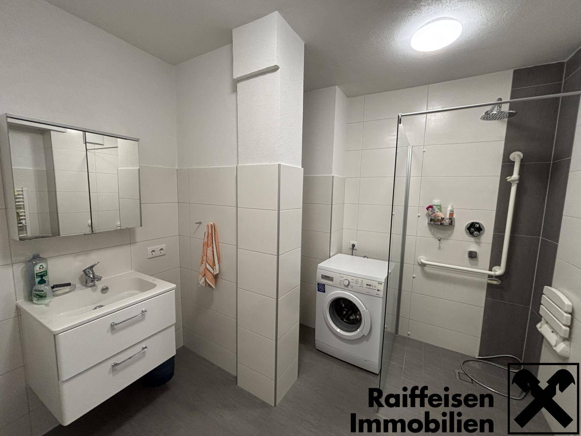 Modernisiertes Badezimmer mit ebenerdiger Dusche, Waschmaschine und Haltegriffen.