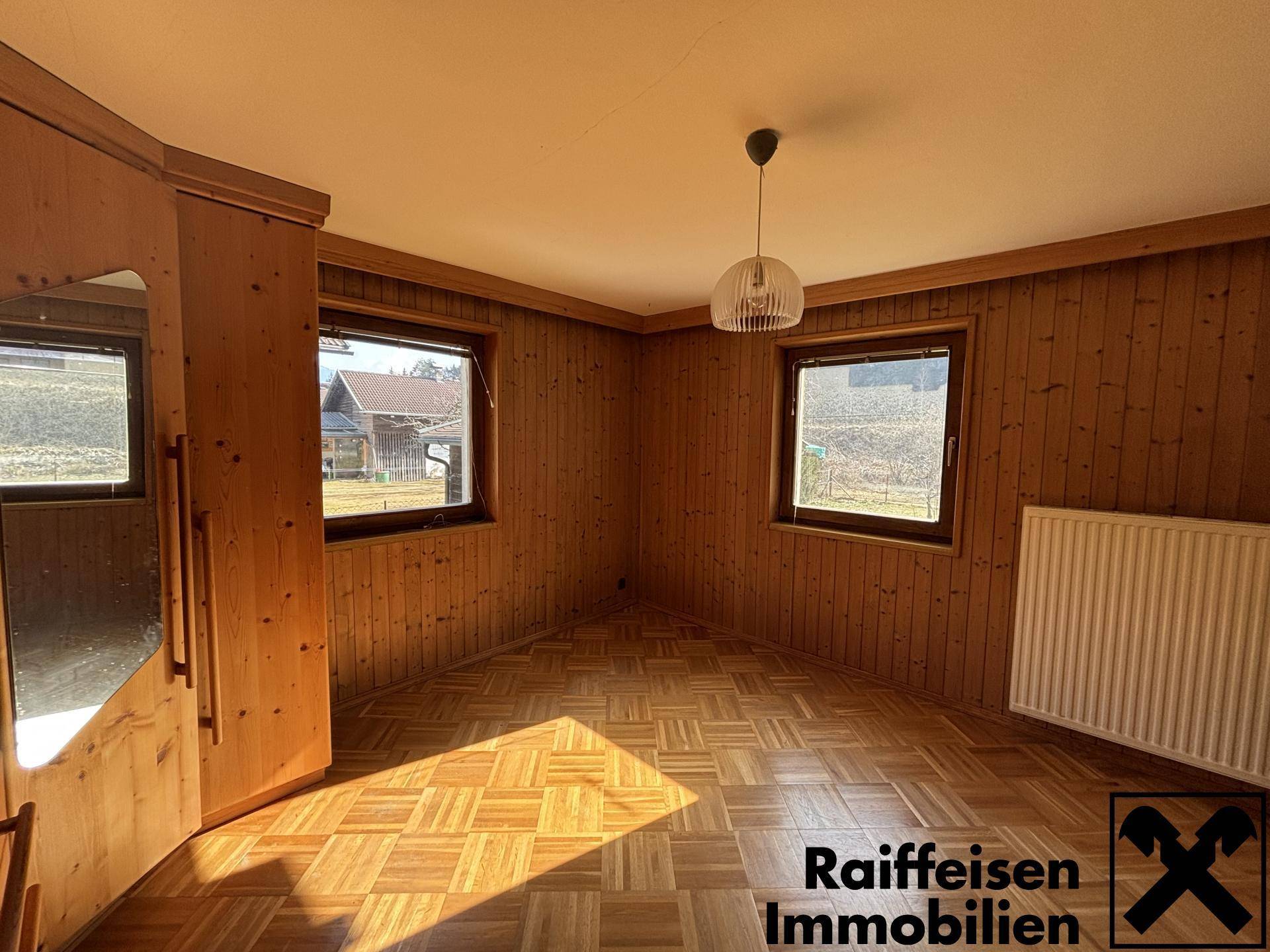 Helles Schlafzimmer mit Holzvertäfelung, Laminatboden und zwei Fenstern.