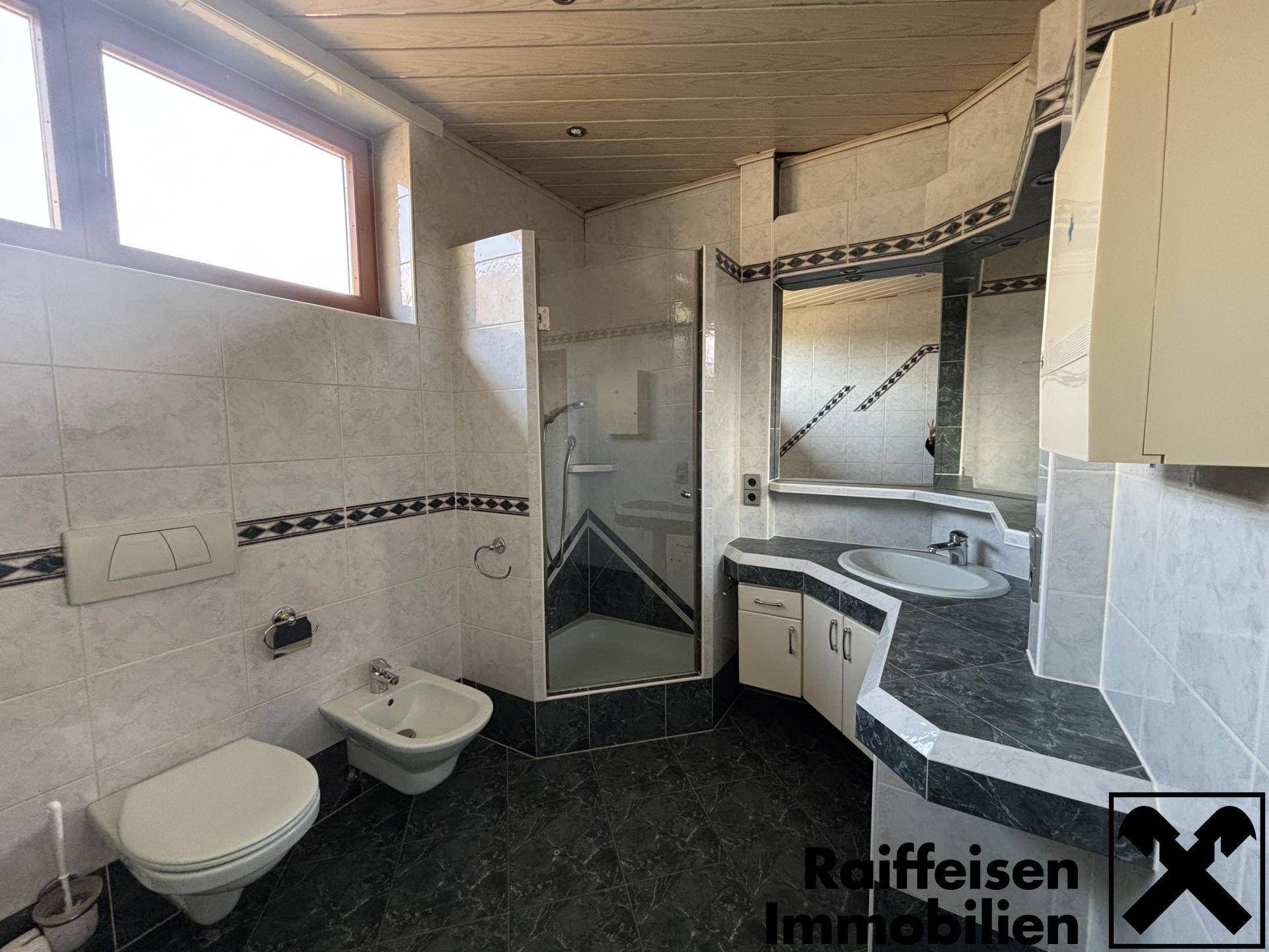 Modern gefliestes Badezimmer mit Duschkabine, WC, Bidet und Doppelwaschbecken.
