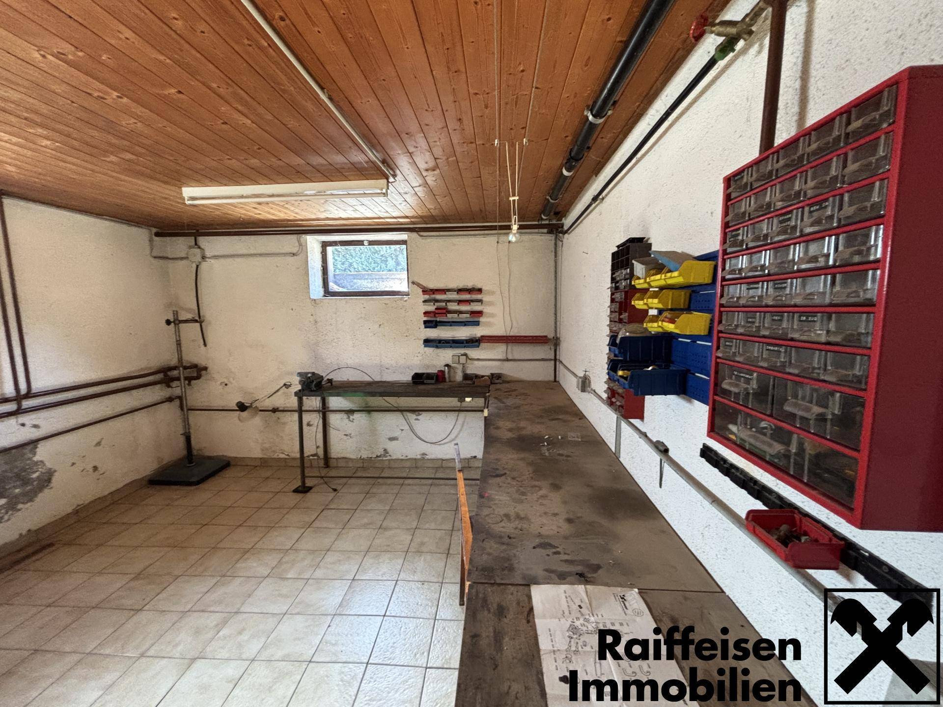 Geräumige Werkstatt im Keller mit Fliesenboden, Holzdecke und praktischen Regalen.
