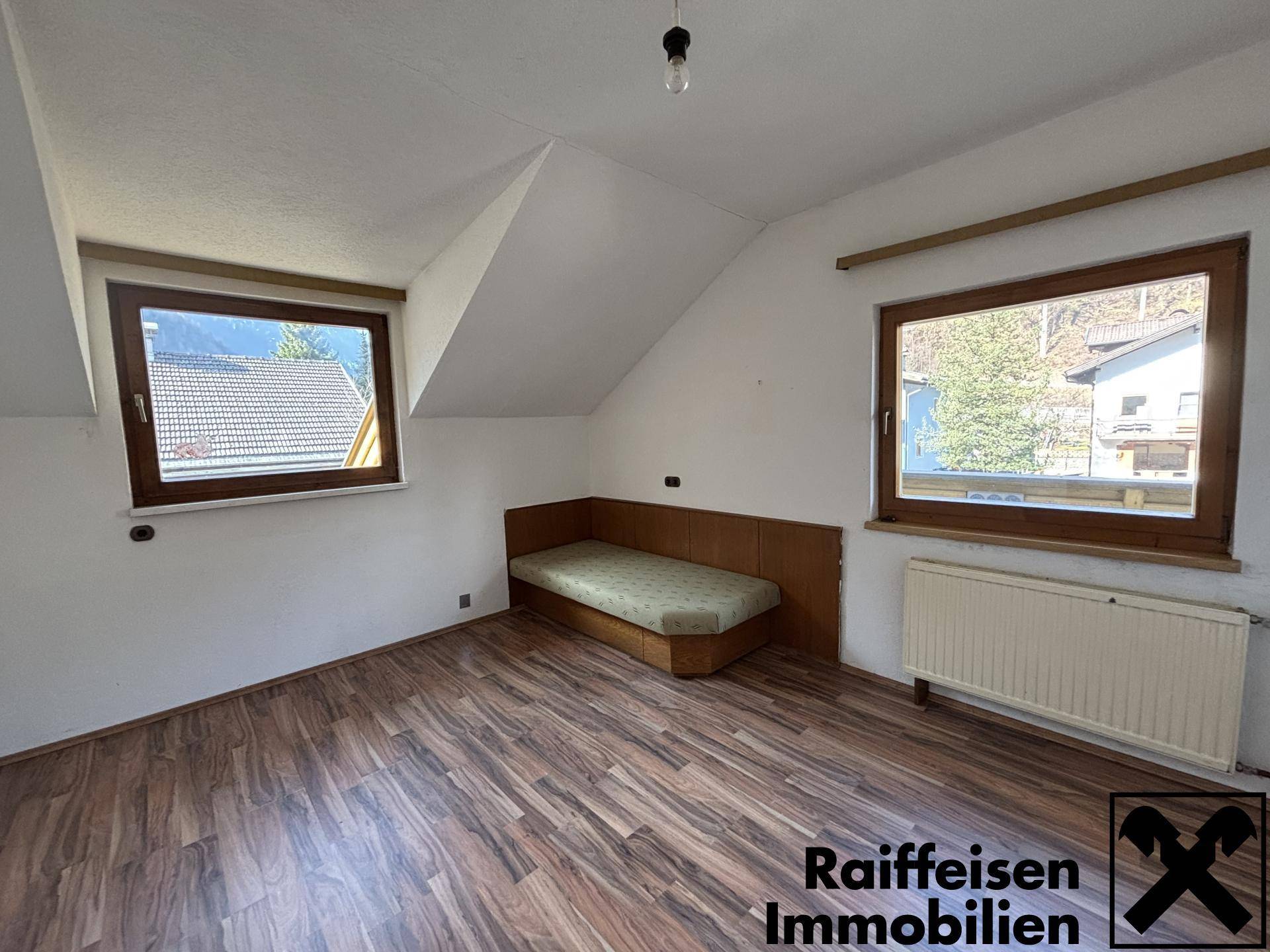 Dachzimmer mit schrägen Wänden, Laminatboden und integrierter Sitzbank.