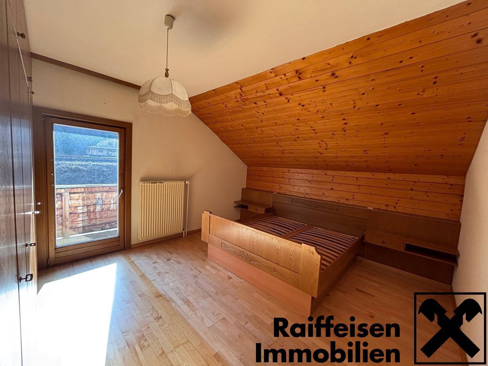 Gemütliches Schlafzimmer im Dachgeschoss mit Holzdecke und Balkonzugang.