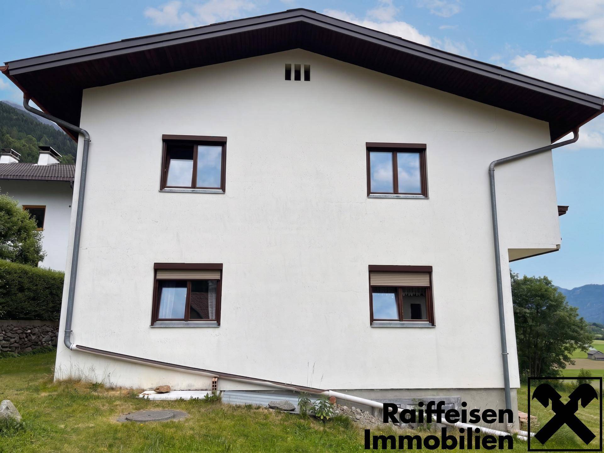 Seitenansicht des Hauses mit weißer Fassade, braunen Fenstern und einem klassischen Satteldach.