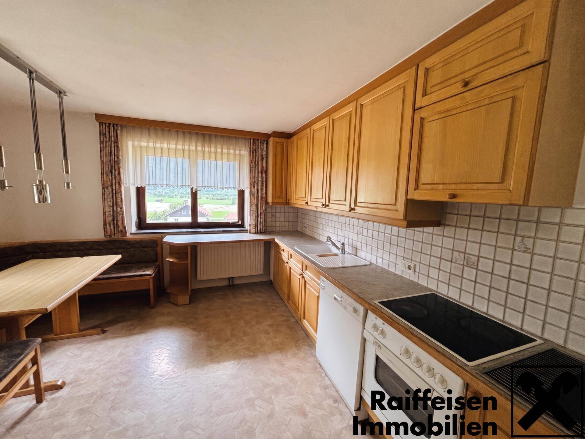 Gemütliche Küche mit Holzschränken, Essbereich und Fenster mit weitem Blick ins Grüne.