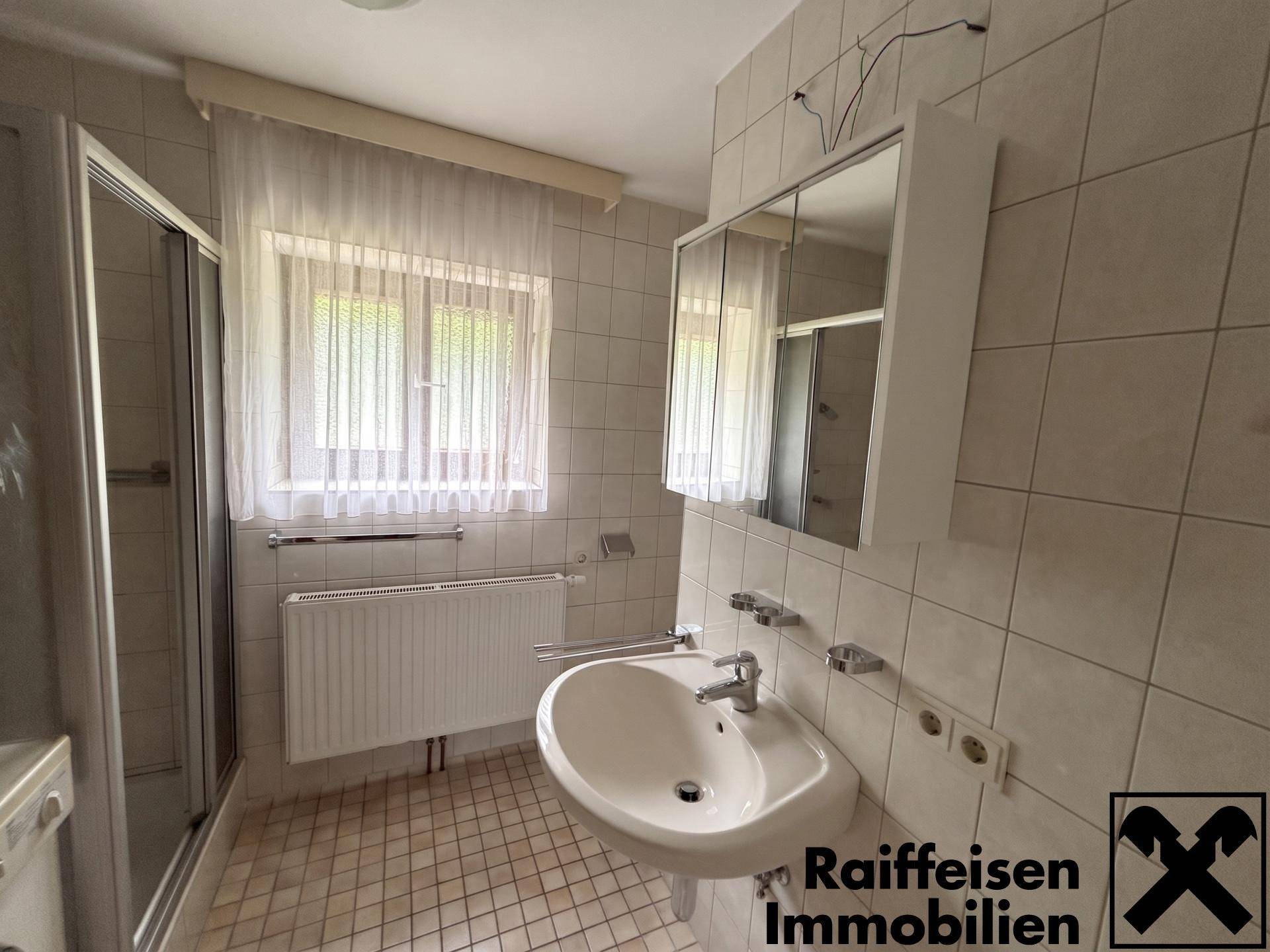 Gefliestes Badezimmer mit Duschkabine, Waschbecken und Fenster für natürliches Tageslicht.