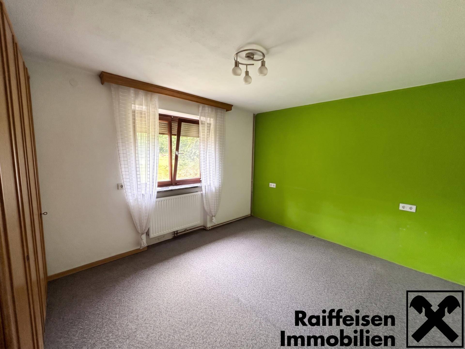 Schlafzimmer mit grün gestrichener Akzentwand, Teppichboden und Fenster mit Blick ins Grüne.