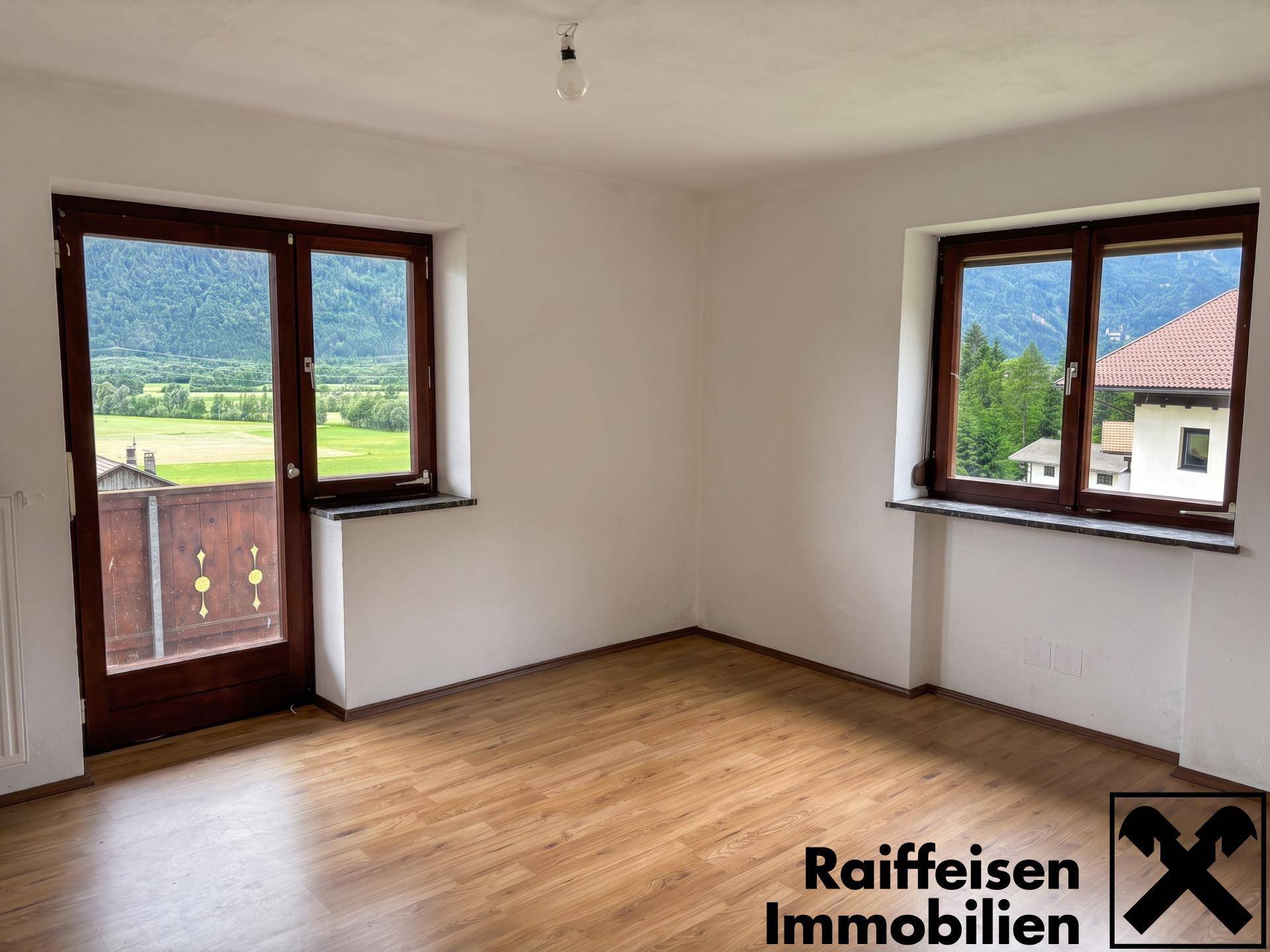 Heller Raum mit Laminatboden und Zugang zu einem Balkon, mit Bergblick und grüner Umgebung.
