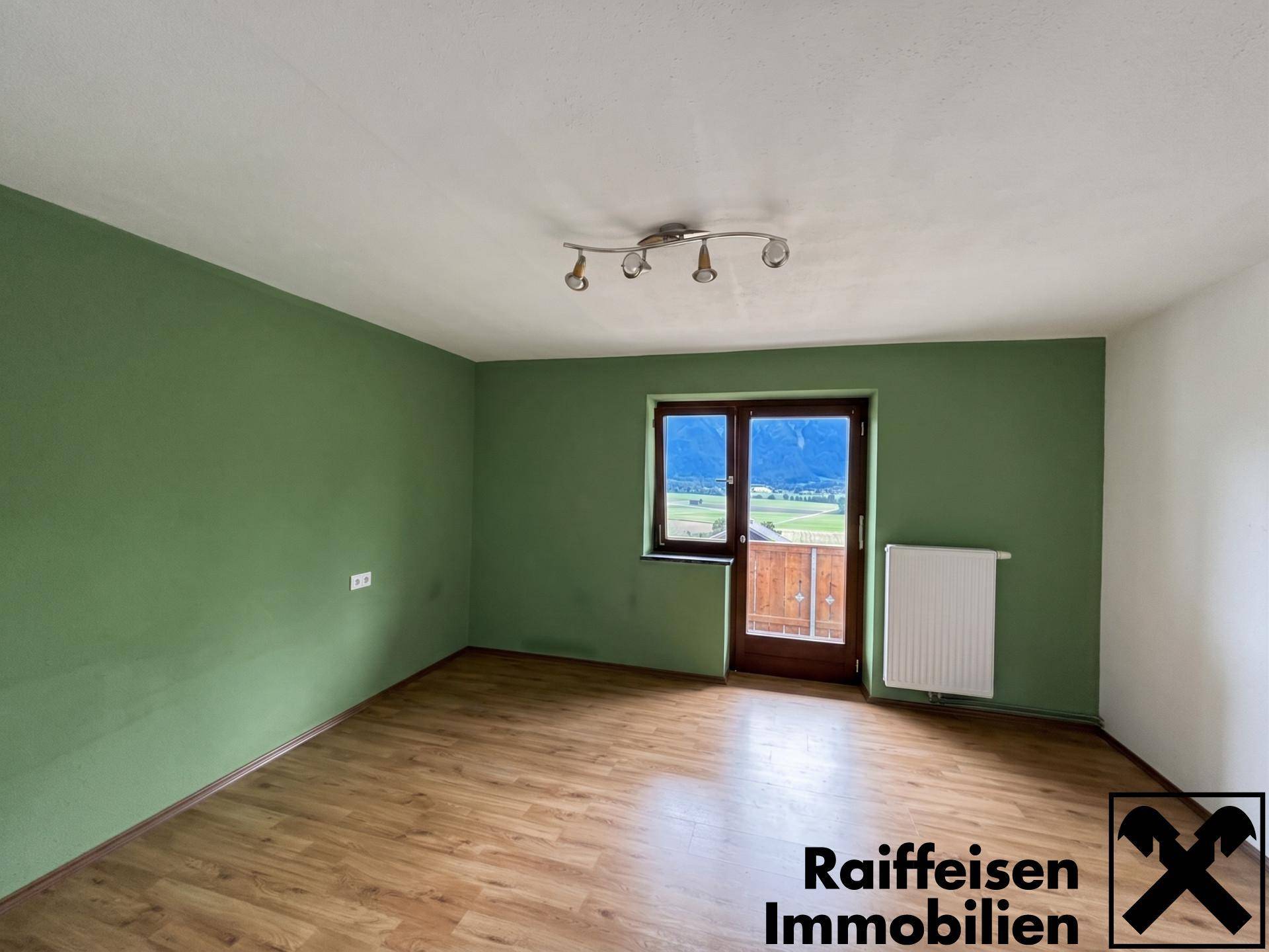 Raum mit grüner Akzentwand, Laminatboden und Balkonzugang mit Bergblick.