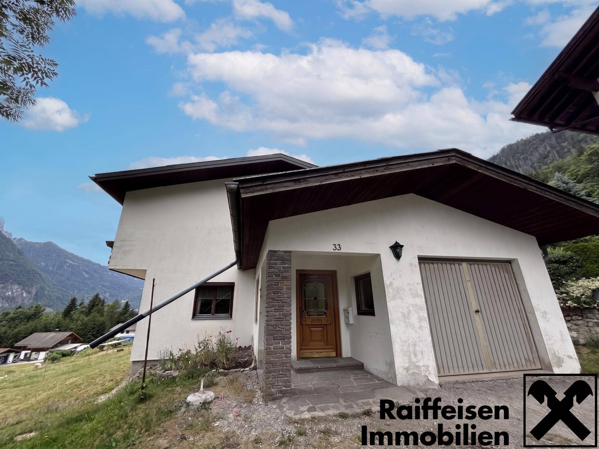 Eingangsbereich des Hauses mit Holztür und angrenzender Garage, eingebettet in die Naturkulisse.