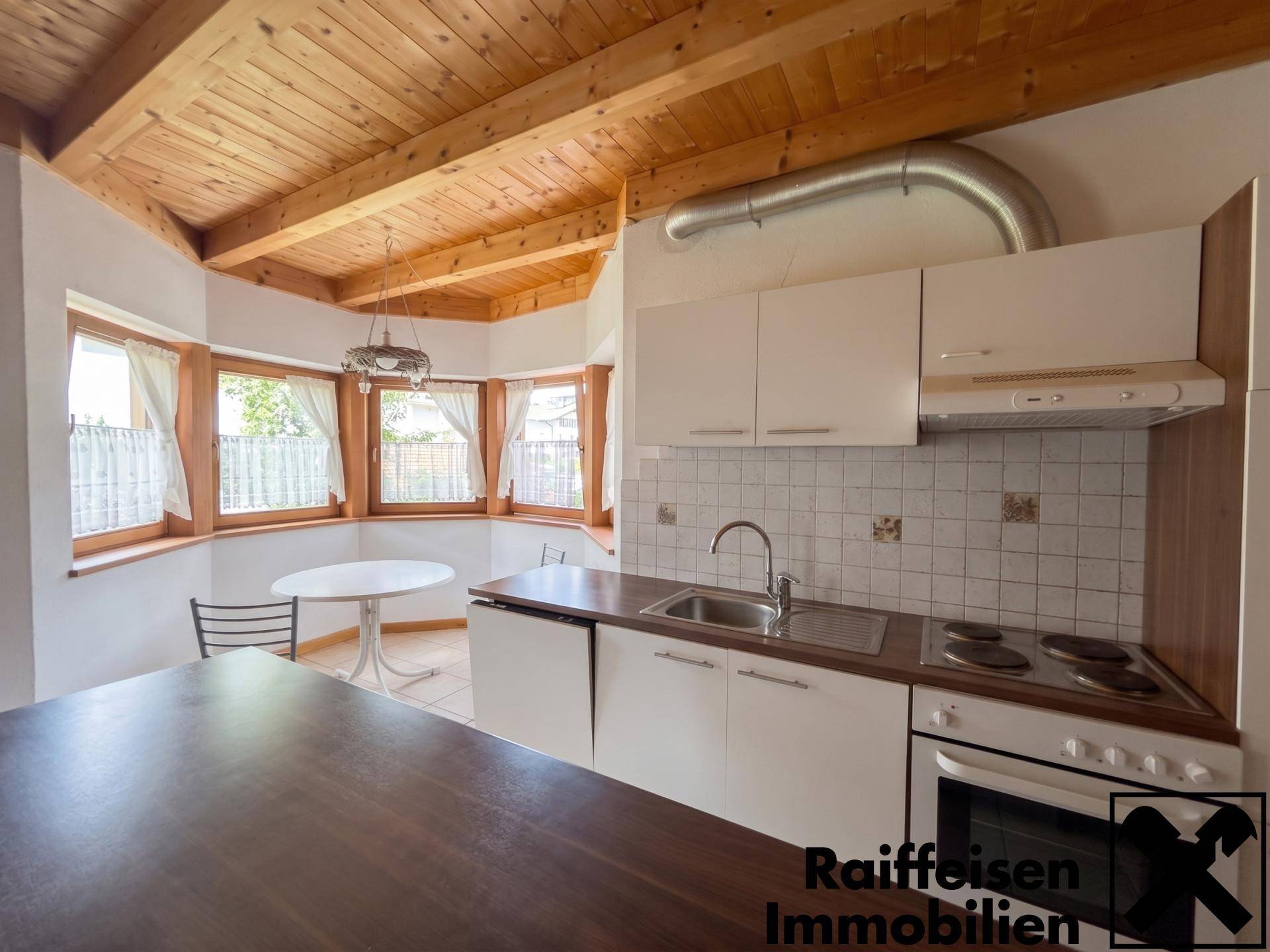 Funktionale Küche mit Holzbalkendecke, Essbereich und Blick ins Grüne durch mehrere Fenster.