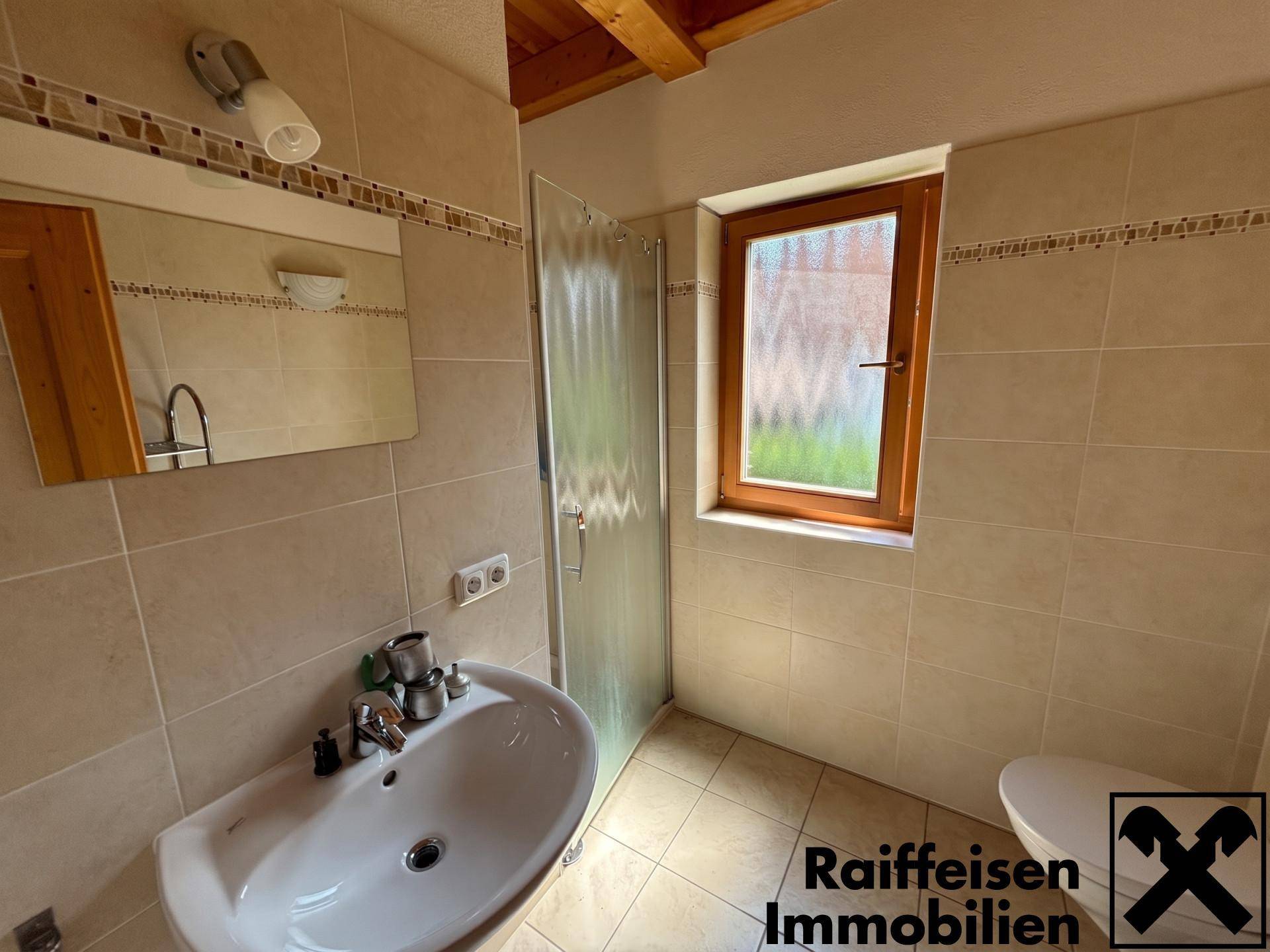 Badezimmer mit beigefarbenen Fliesen, Dusche und Fenster für Tageslicht.