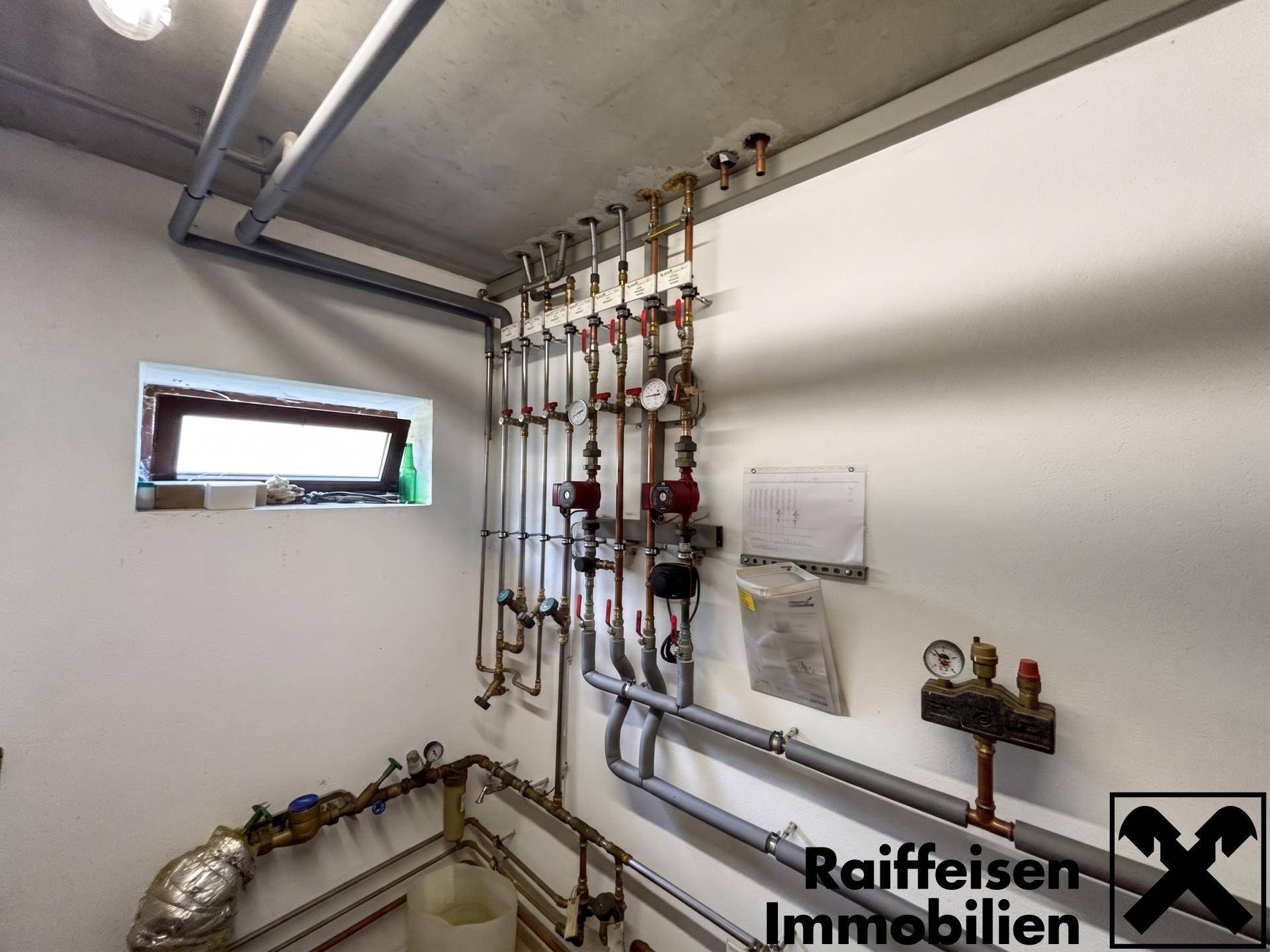 Heizungsraum mit komplexer Rohrinstallation und kleinem Fenster.