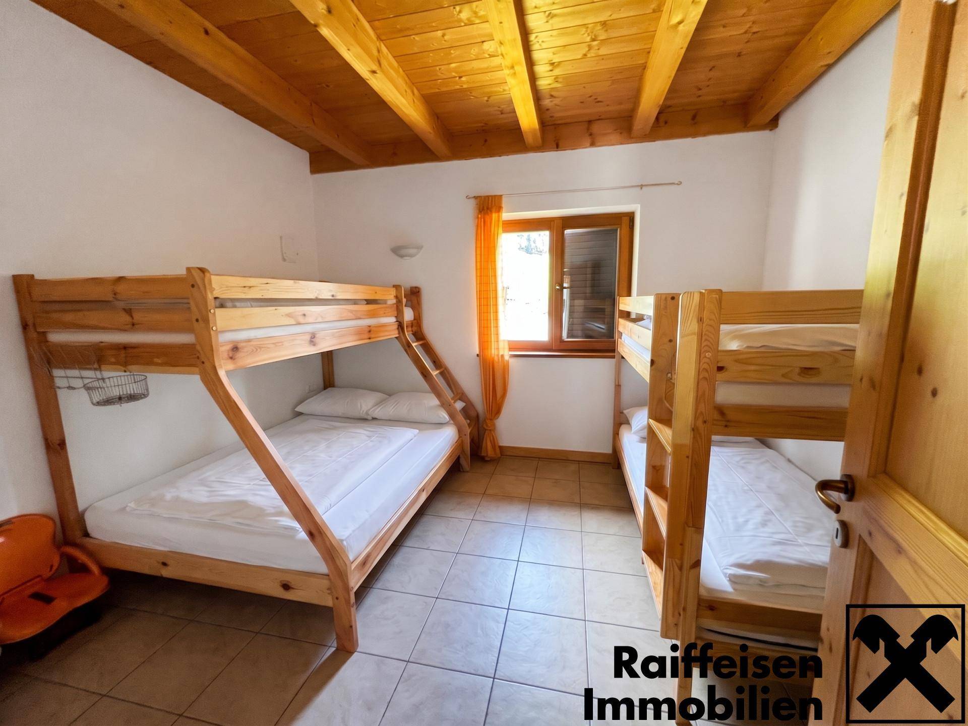 Kinderzimmer mit zwei Etagenbetten, Fliesenboden und Holzbalkendecke.