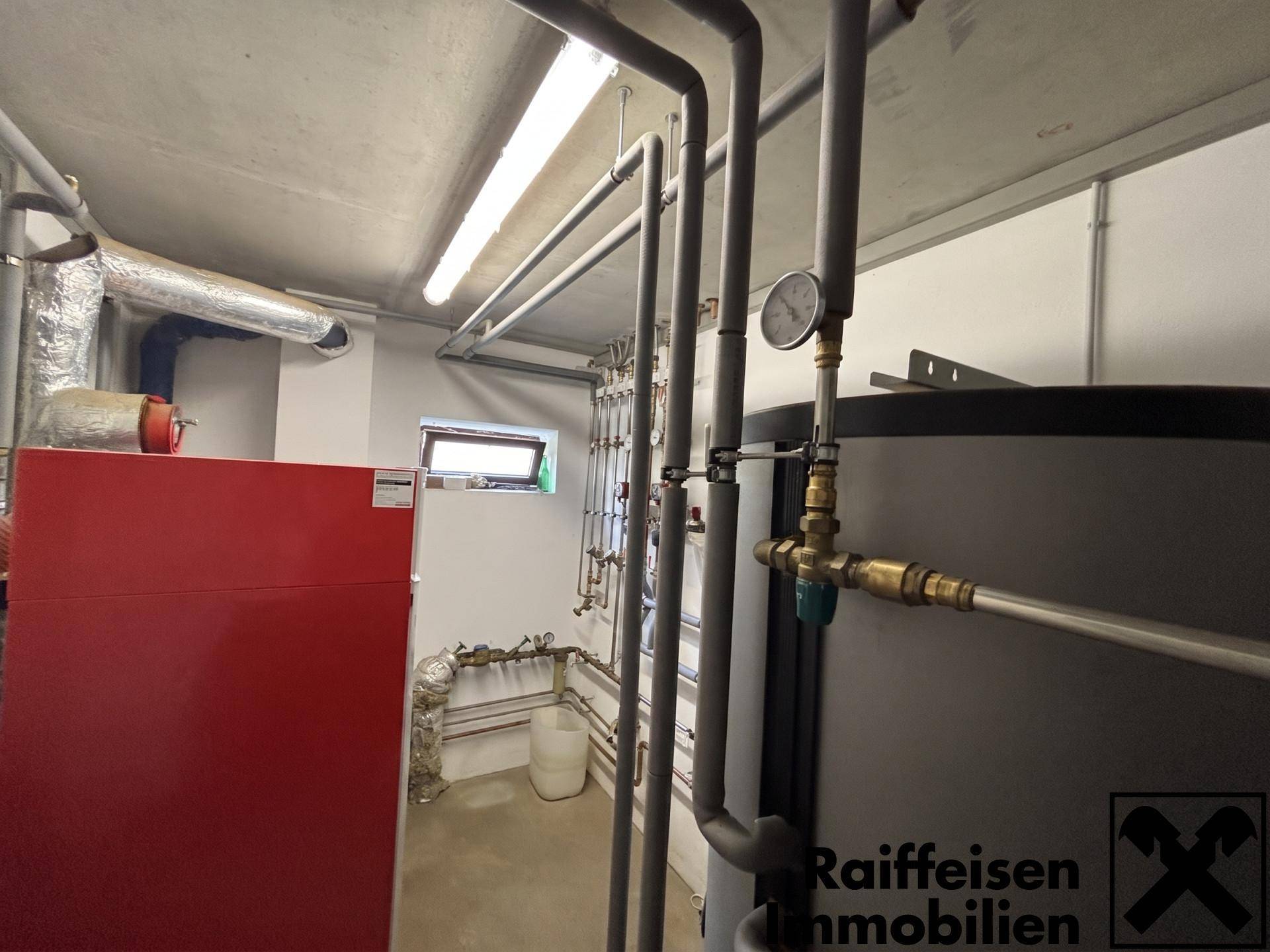 Technikraum mit Heizkessel, Warmwasserspeicher und sichtbaren Rohrleitungen.