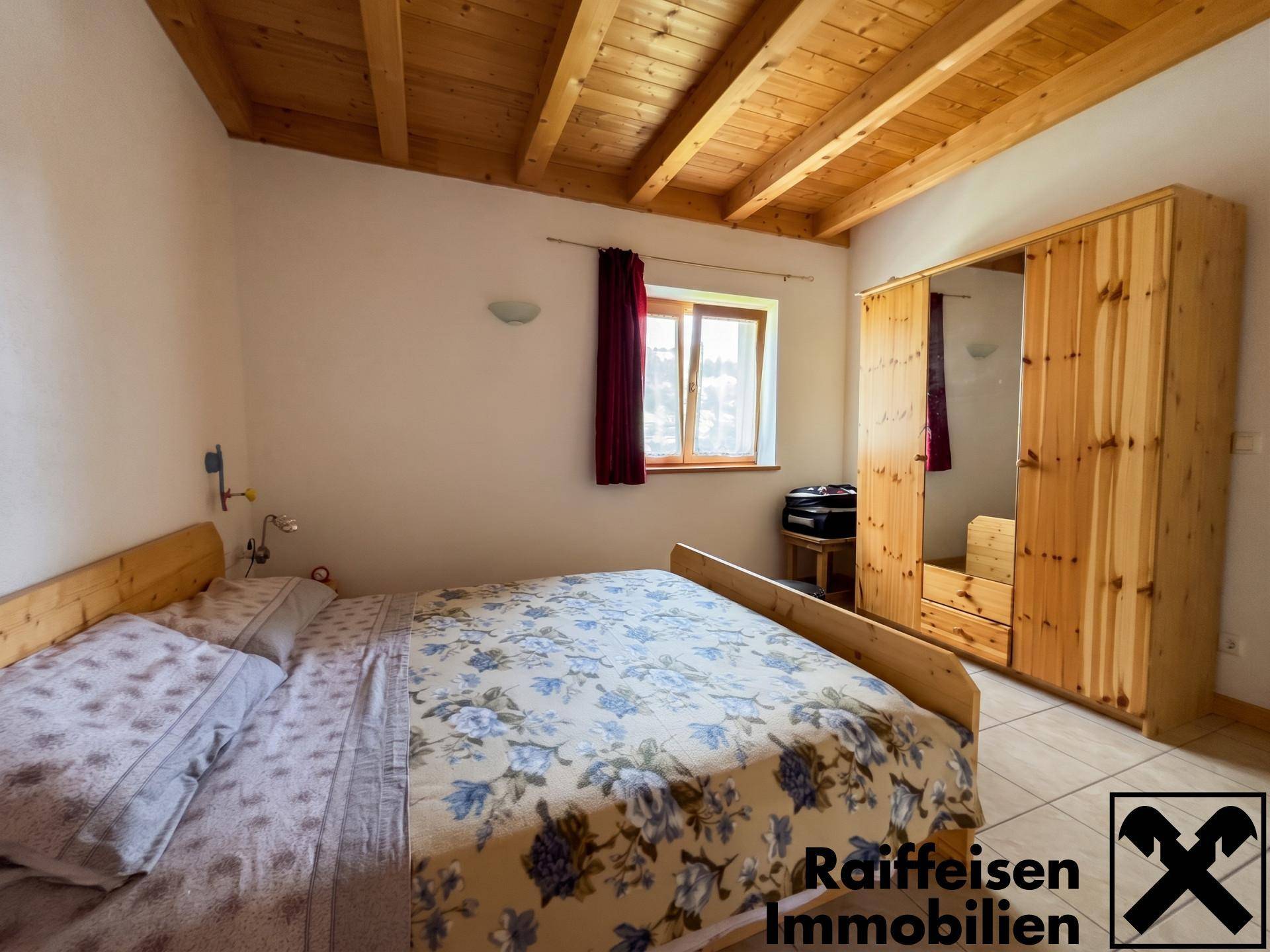 Gemütliches Schlafzimmer mit Holzbalkendecke, Fliesenboden und großem Holzschrank.