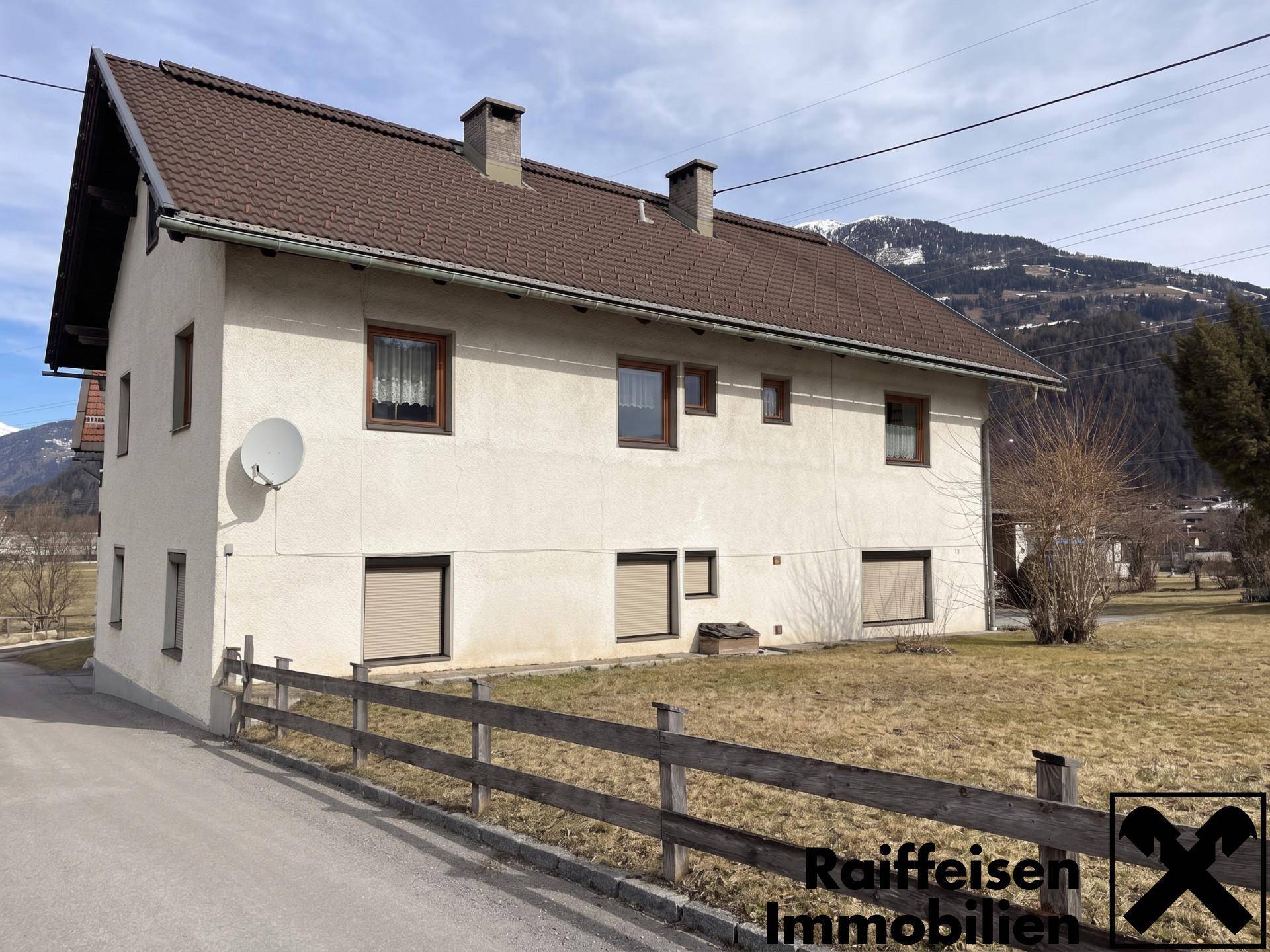 Rückansicht des Wohnhauses mit braunem Ziegeldach und Schornsteinen vor alpiner Kulisse.