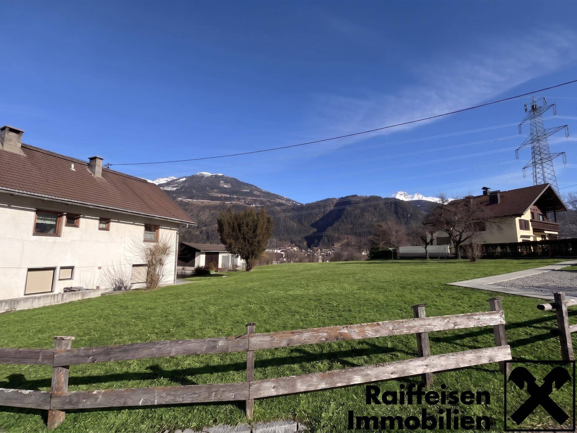 Weitläufige Rasenfläche des Anwesens mit Blick auf die umliegenden Berge und Nachbarhäuser.
