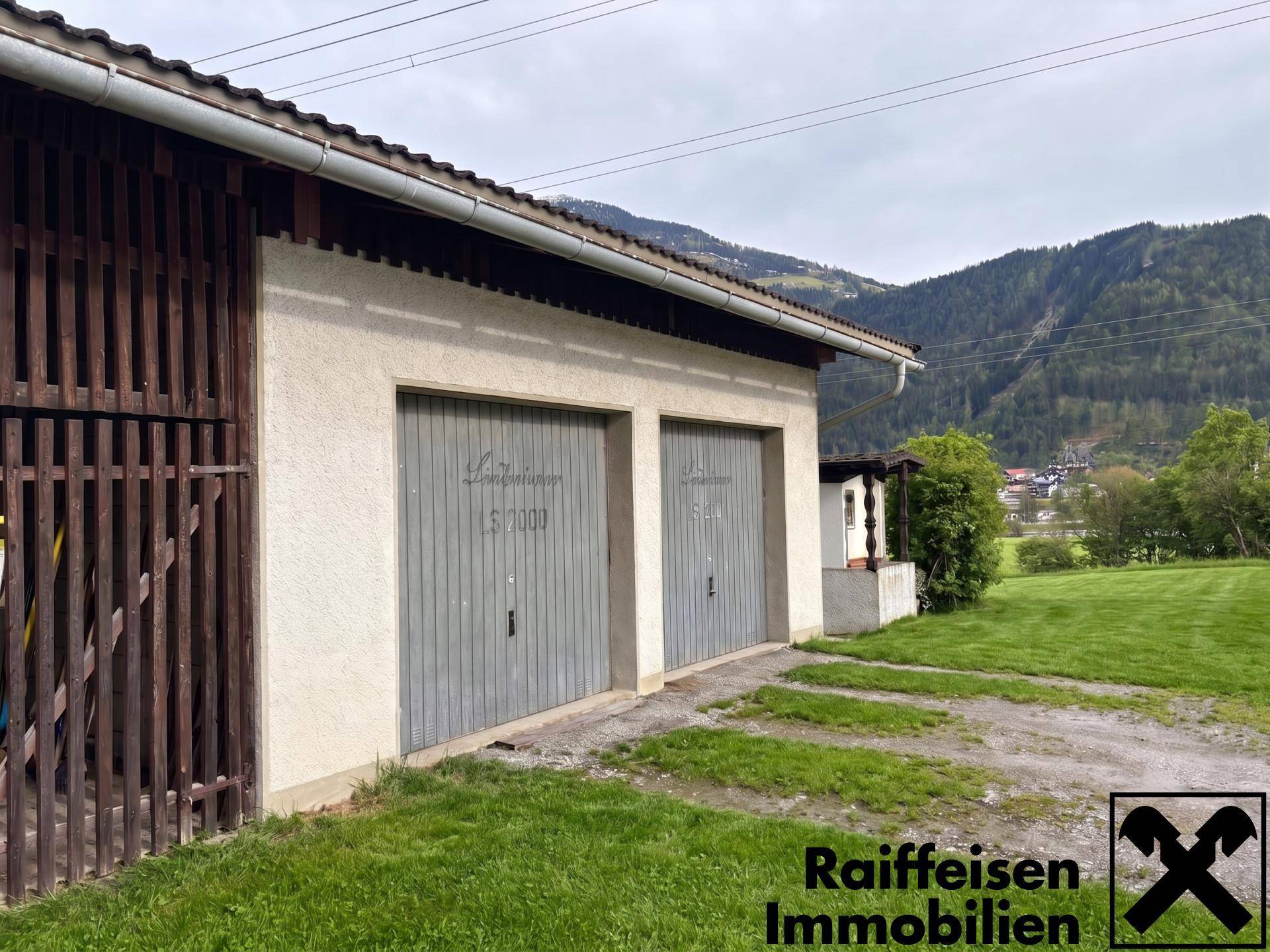 Doppelgarage mit zwei grauen Toren und einem Satteldach, eingebettet in eine grüne Landschaft.