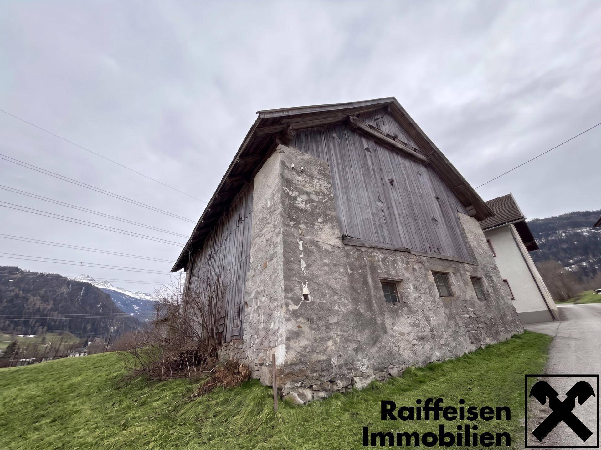 Seitenansicht des rustikalen Holzgebäudes mit verwitterter Fassade und Blick auf die Berge.