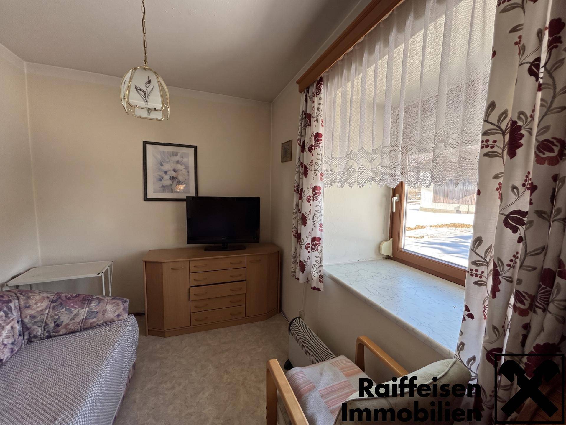Gemütliches Wohnzimmer mit Sofa, Fernseher und einem Fenster mit Vorhängen.