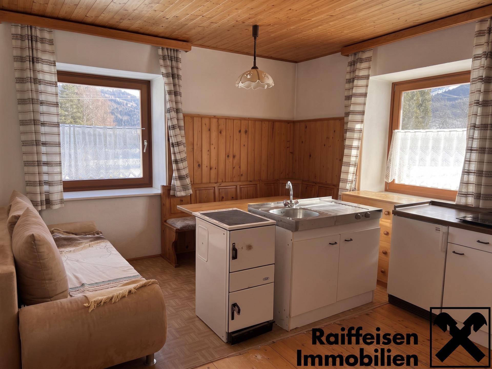 Rustikaler Wohn-Essbereich mit Holztäfelung, kleiner Küchenzeile und gemütlicher Sitzecke.