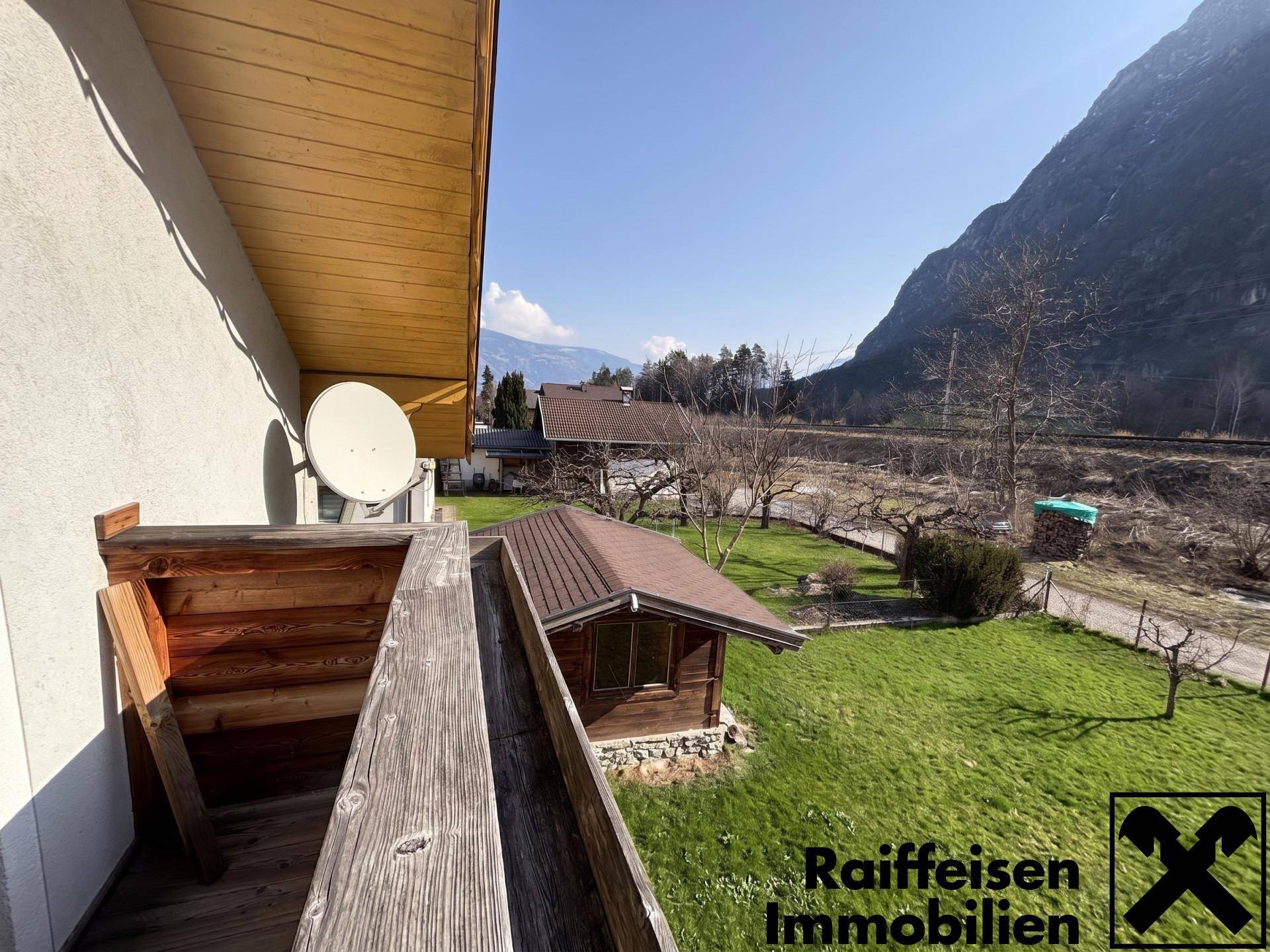 Balkon mit weitem Blick über den Garten, eine Gartenhütte und die Berglandschaft.