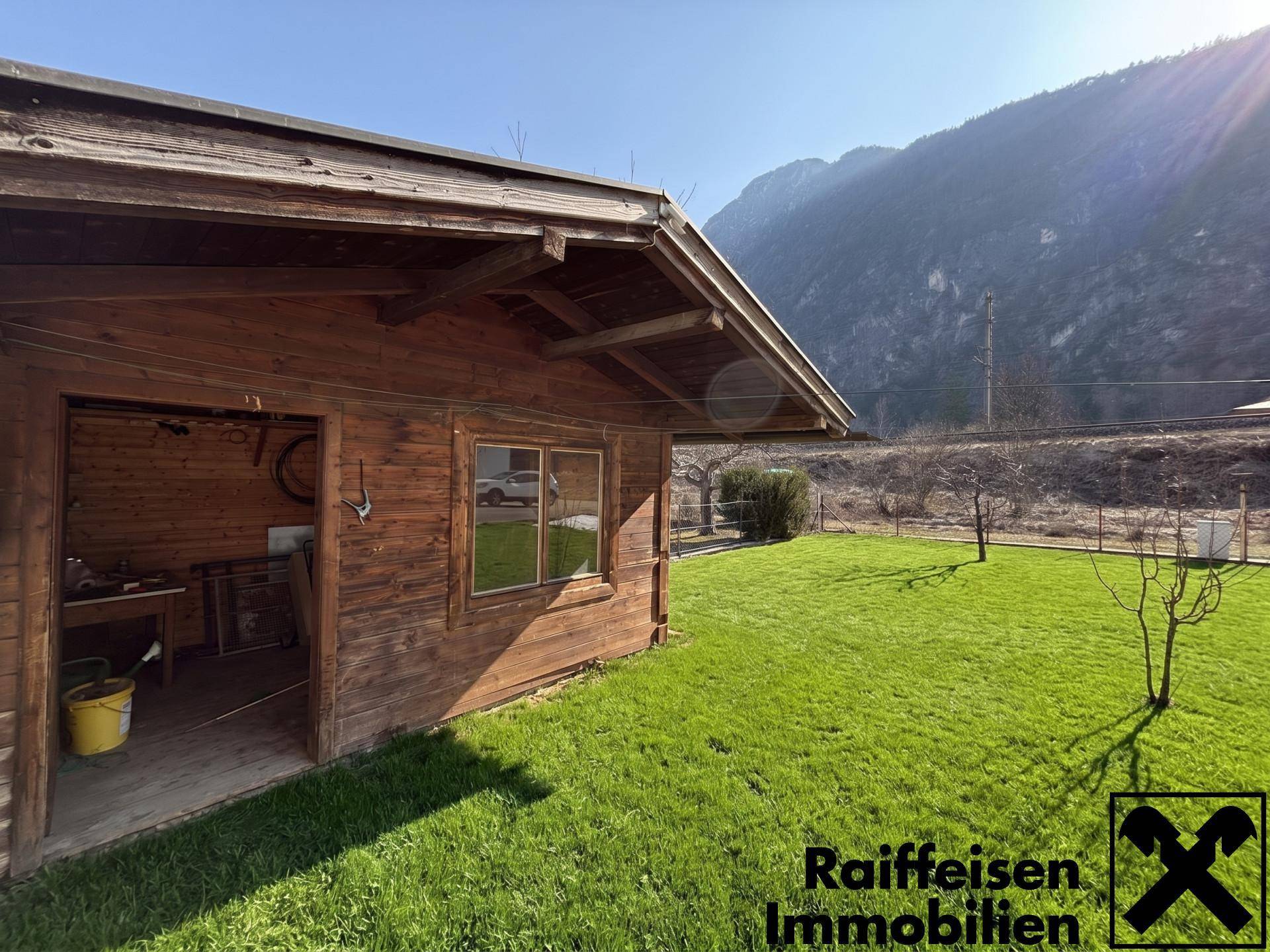 Rustikale Gartenhütte aus Holz auf einer grünen Wiese mit Bergblick.