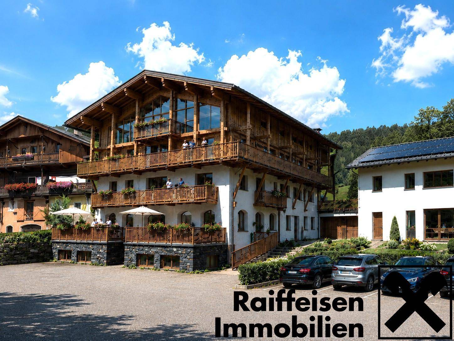 Mehrstöckiges Gebäude mit Holzverkleidung und Balkonen, umgeben von Natur und mit Parkplätzen.