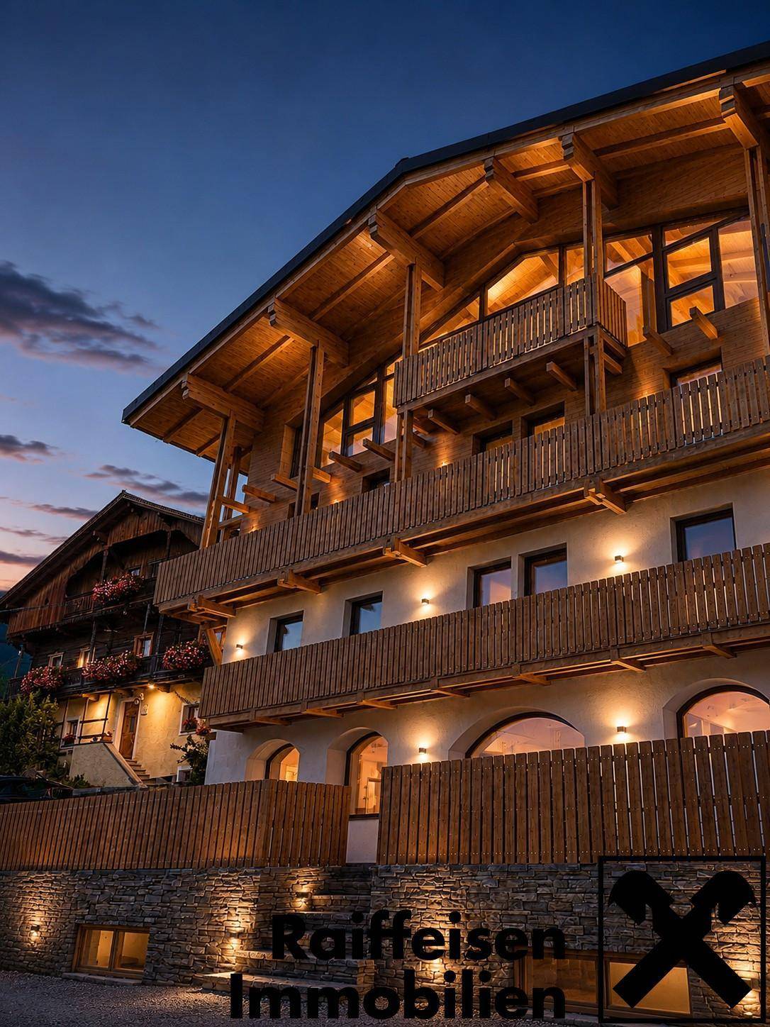 Gebäude im alpinen Stil bei Sonnenuntergang, beleuchtet mit warmem Licht und Holzbalkonen.