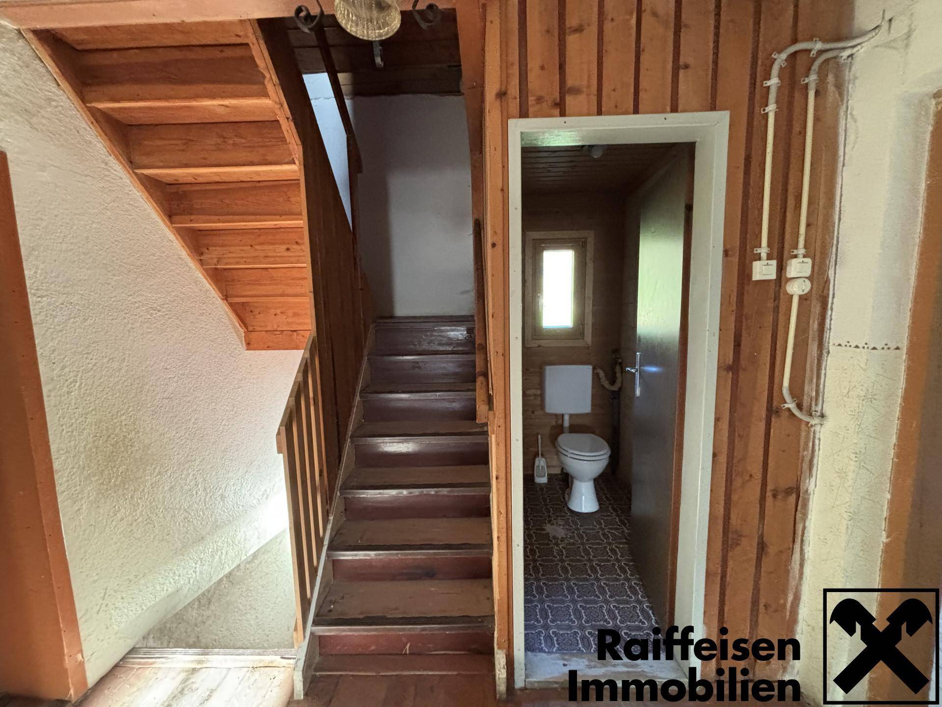 Rustikaler Treppenaufgang aus Holz neben einem kleinen Gäste-WC mit gemustertem Boden.
