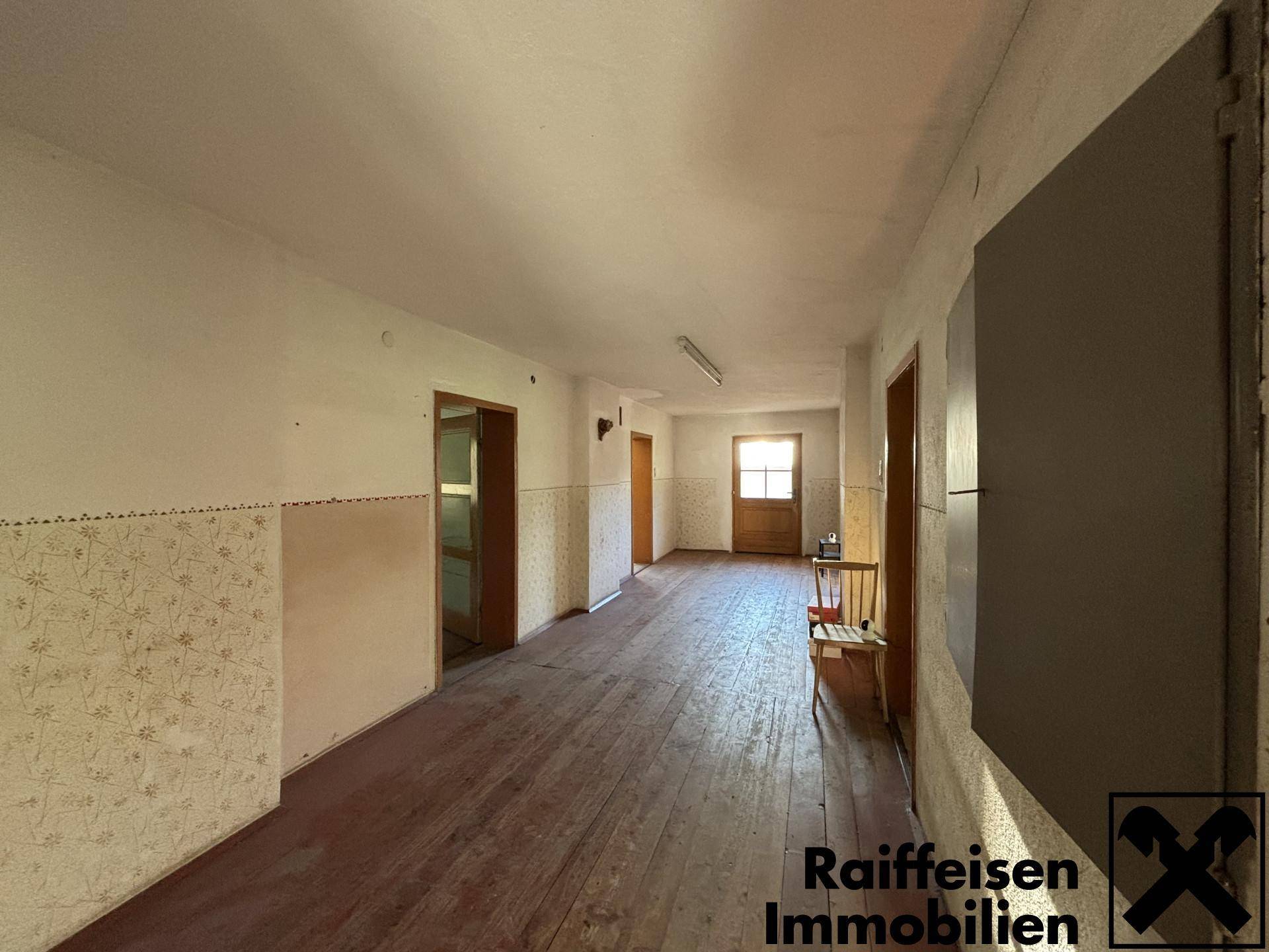 Langer Flur mit Holzdielenboden, gemusterter Tapete und mehreren Türen zu den Zimmern.