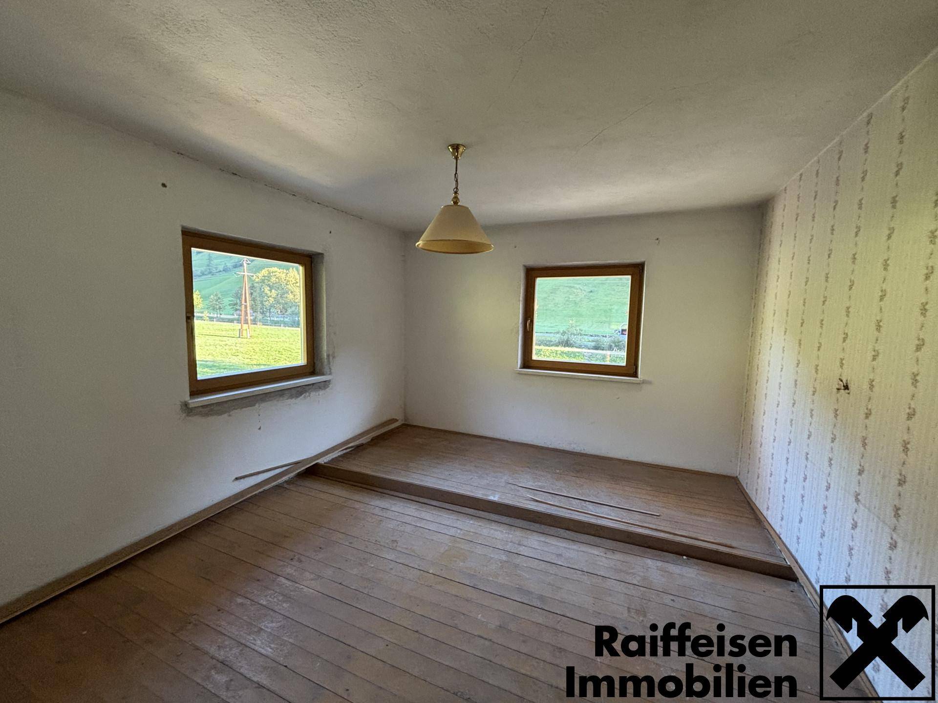 Leeres Schlafzimmer mit Holzdielenboden, zwei Fenstern und einfacher Tapetendekoration.