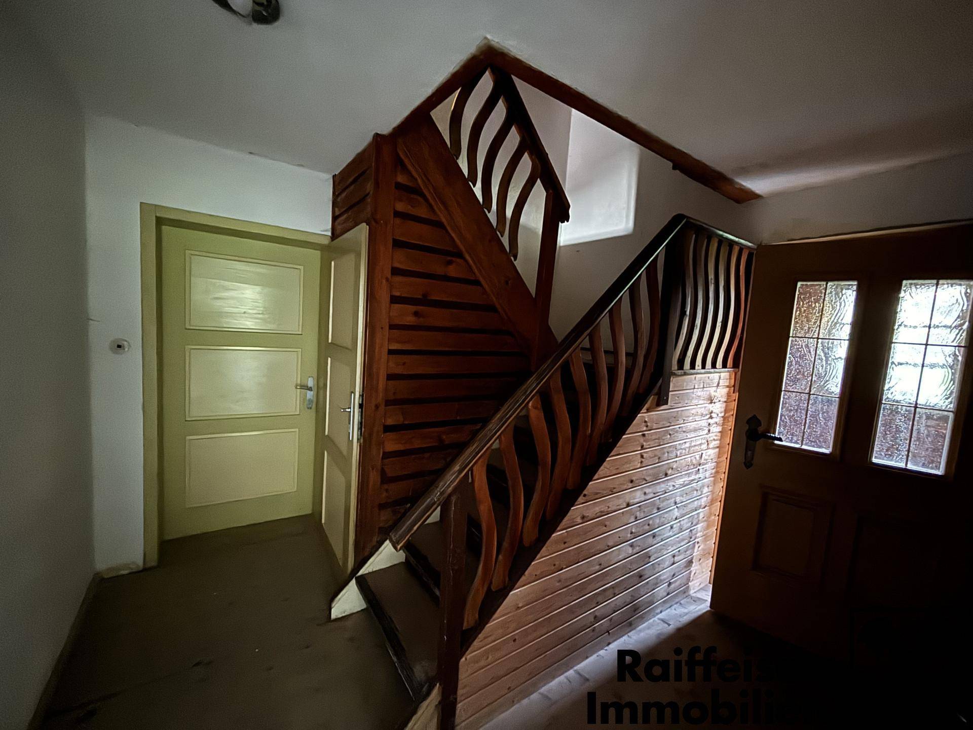 Heller Treppenaufgang aus Holz mit rustikalem Geländer und verschiedenen Zimmertüren.