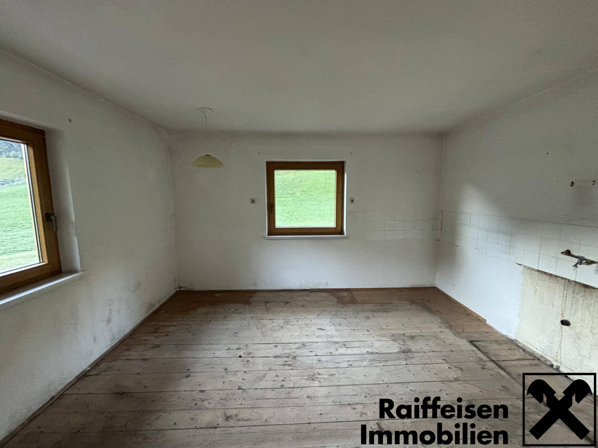 Geräumiger Raum mit Holzdielenboden und gefliester Wand, vorbereitet für eine Kücheneinrichtung.