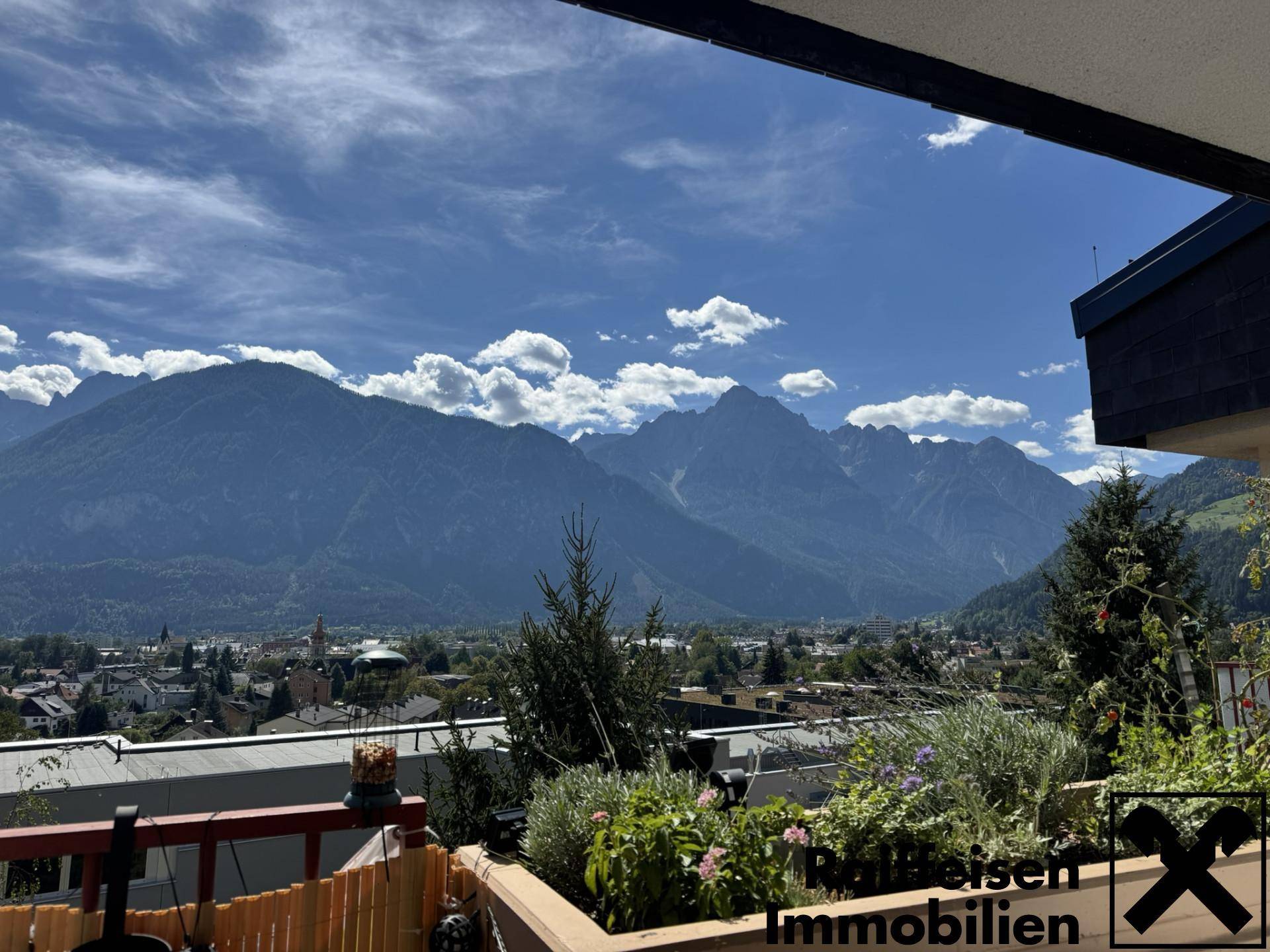 Balkon mit atemberaubendem Bergblick über die Stadt und üppiger Bepflanzung unter blauem Himmel.