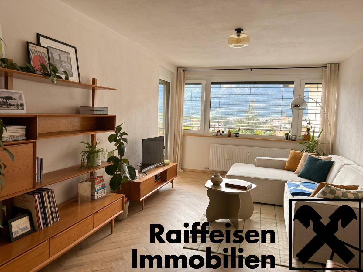 Helles Wohnzimmer mit Holzregal, beigem Sofa und Bergblick durch große Fenster.
